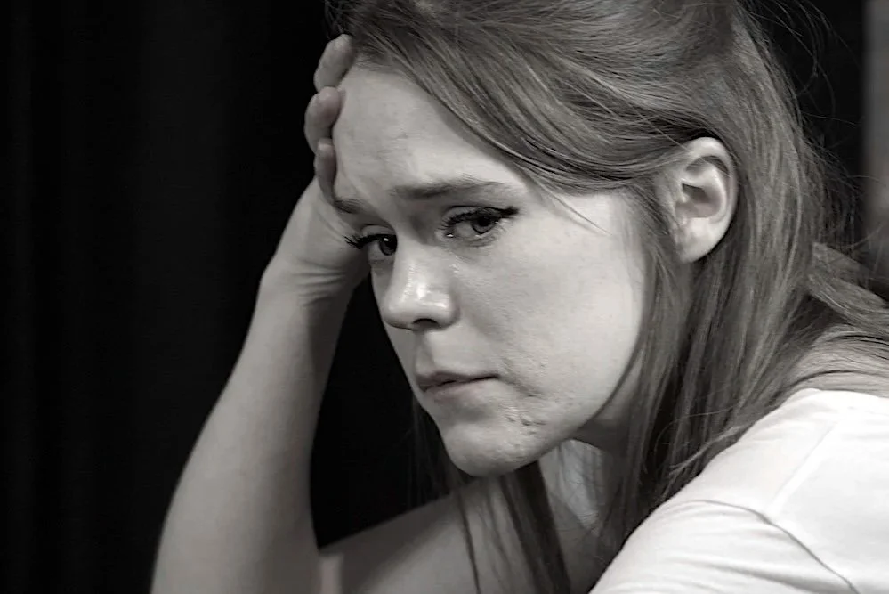A woman with red hair and a pensive expression, resting her head against her hand.