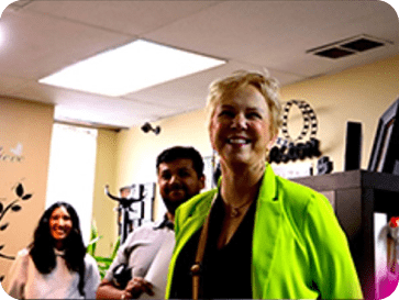 Smiling woman in a bright green blazer in an office with colleagues in the background.
