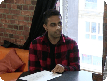 A man sitting at a table near a window with brick wall background, reading a book.