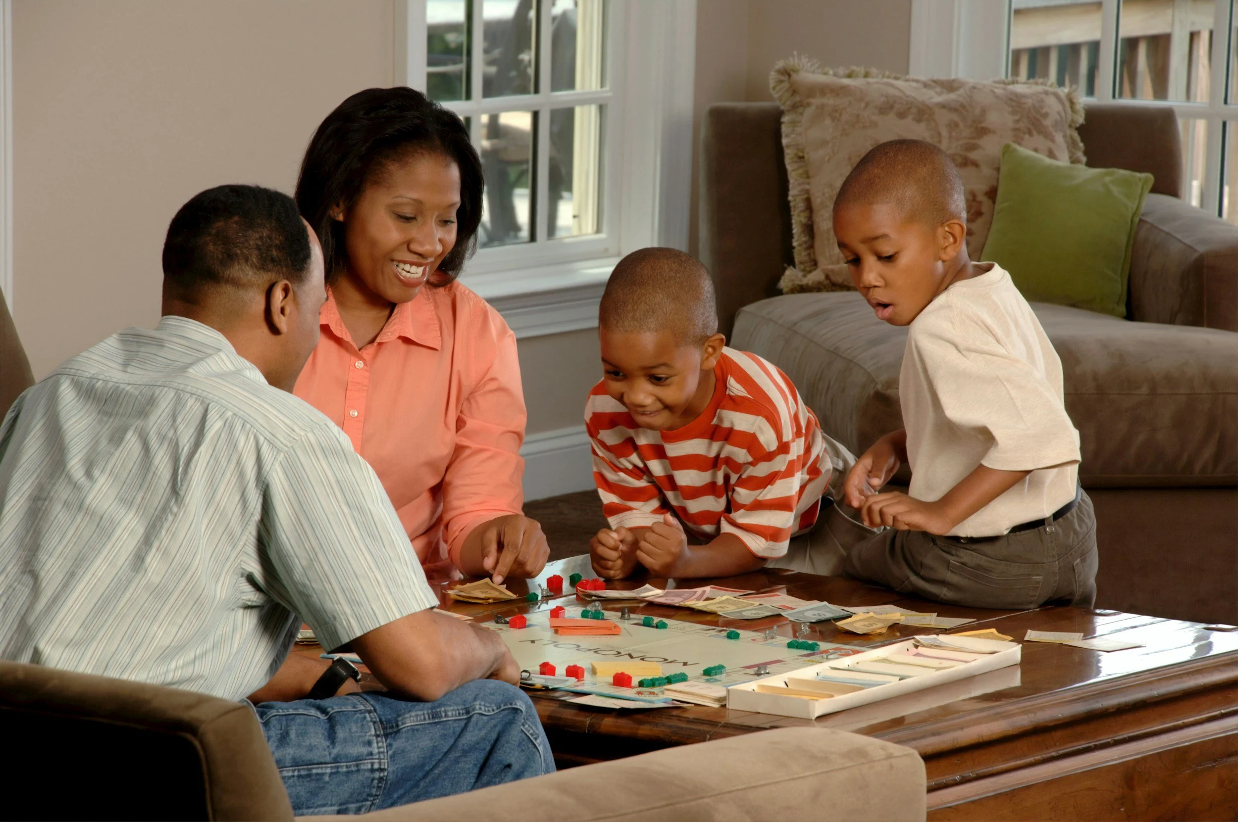 Family playing Monopoly game on a coffee table in the living room.