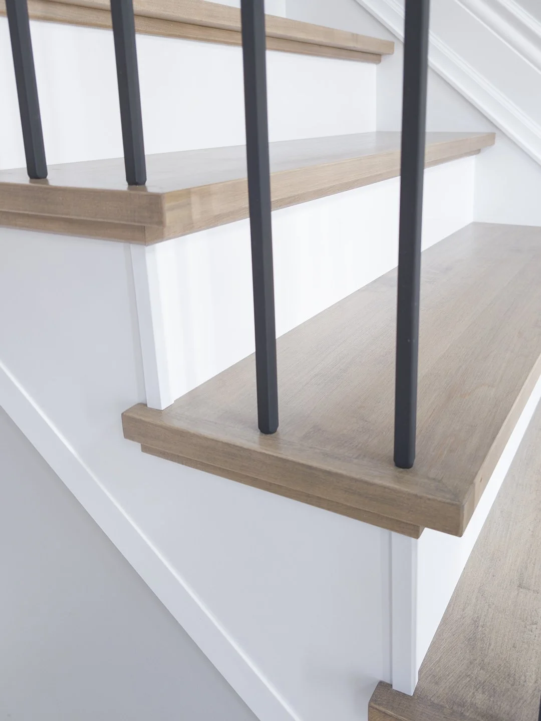 Detail shot of modern, minimalist matte black square metal balusters seamlessly drilled and inserted into the clean edge profile of a grey-toned Canadian hardwood recap stair tread.