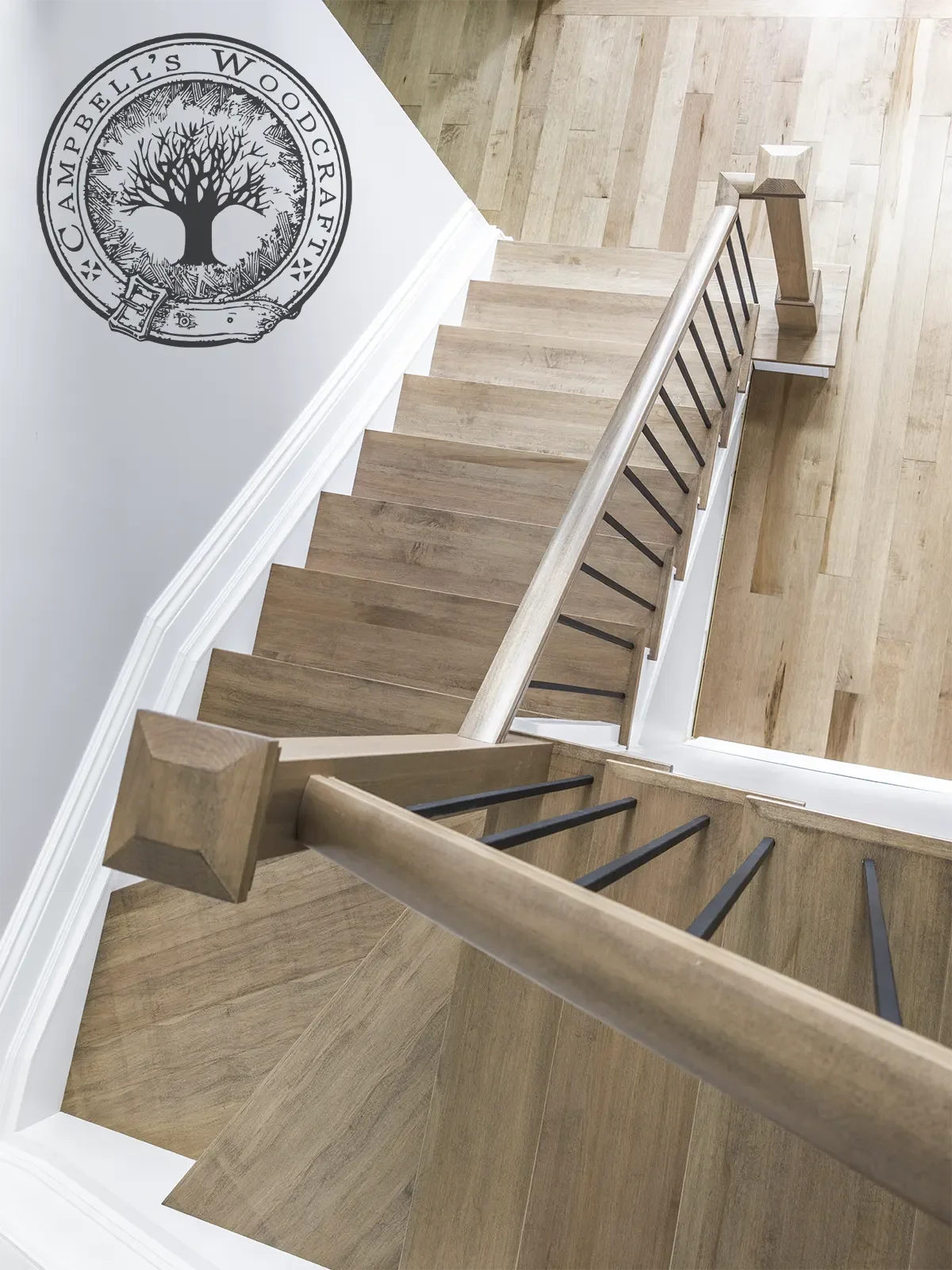 High-angle view of an elegant maple stair (recap) featuring clean hardwood treads, a matching wood handrail, and modern black metal spindles.