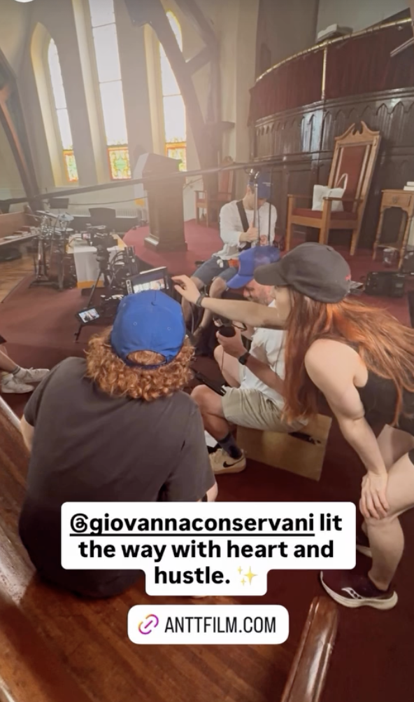 Filming crew on set inside a church with stained glass windows, a raised platform, and wooden chairs, preparing for a scene.