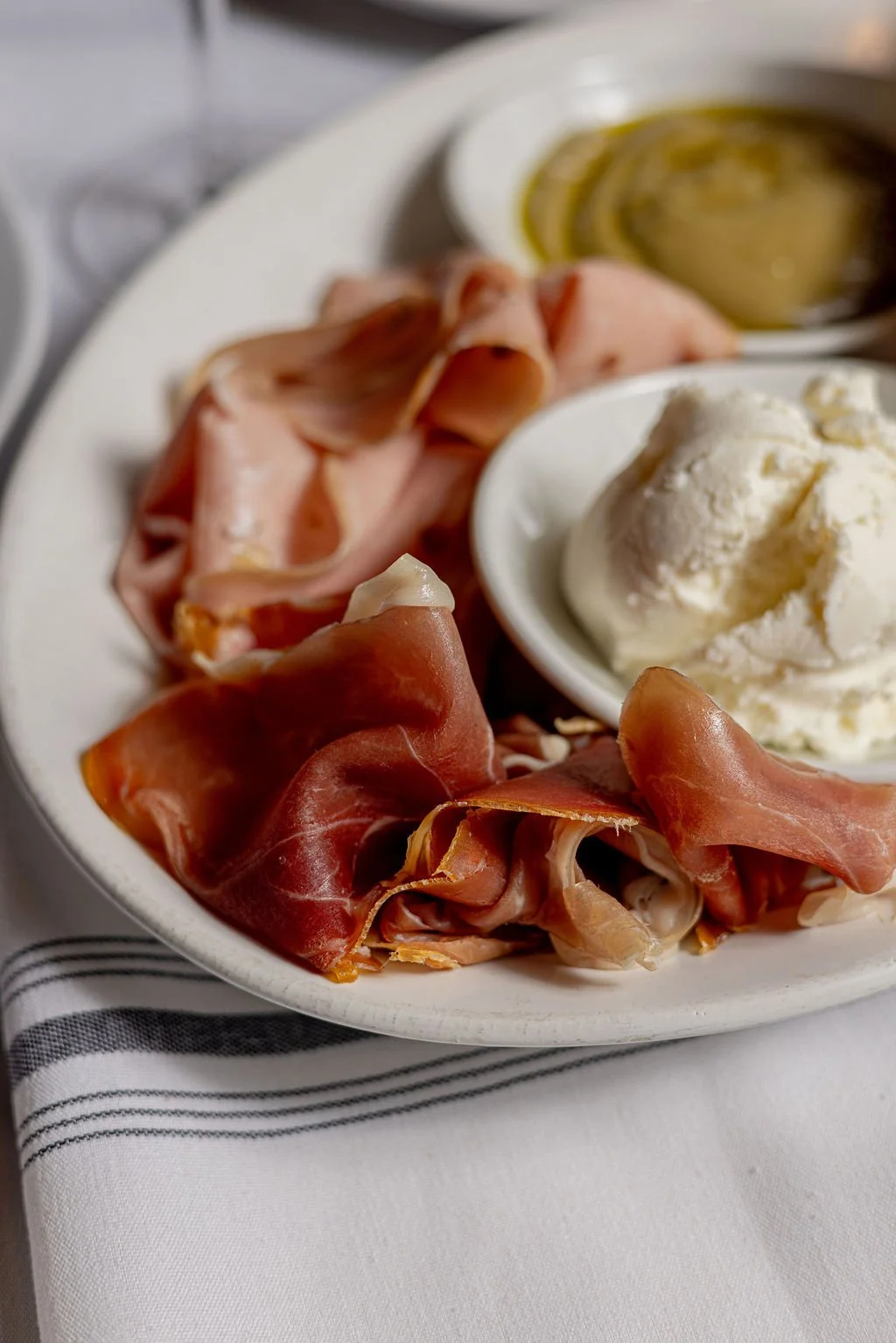 Plate with slices of prosciutto, a scoop of vanilla ice cream, and a small dish of olive oil and balsamic vinegar.