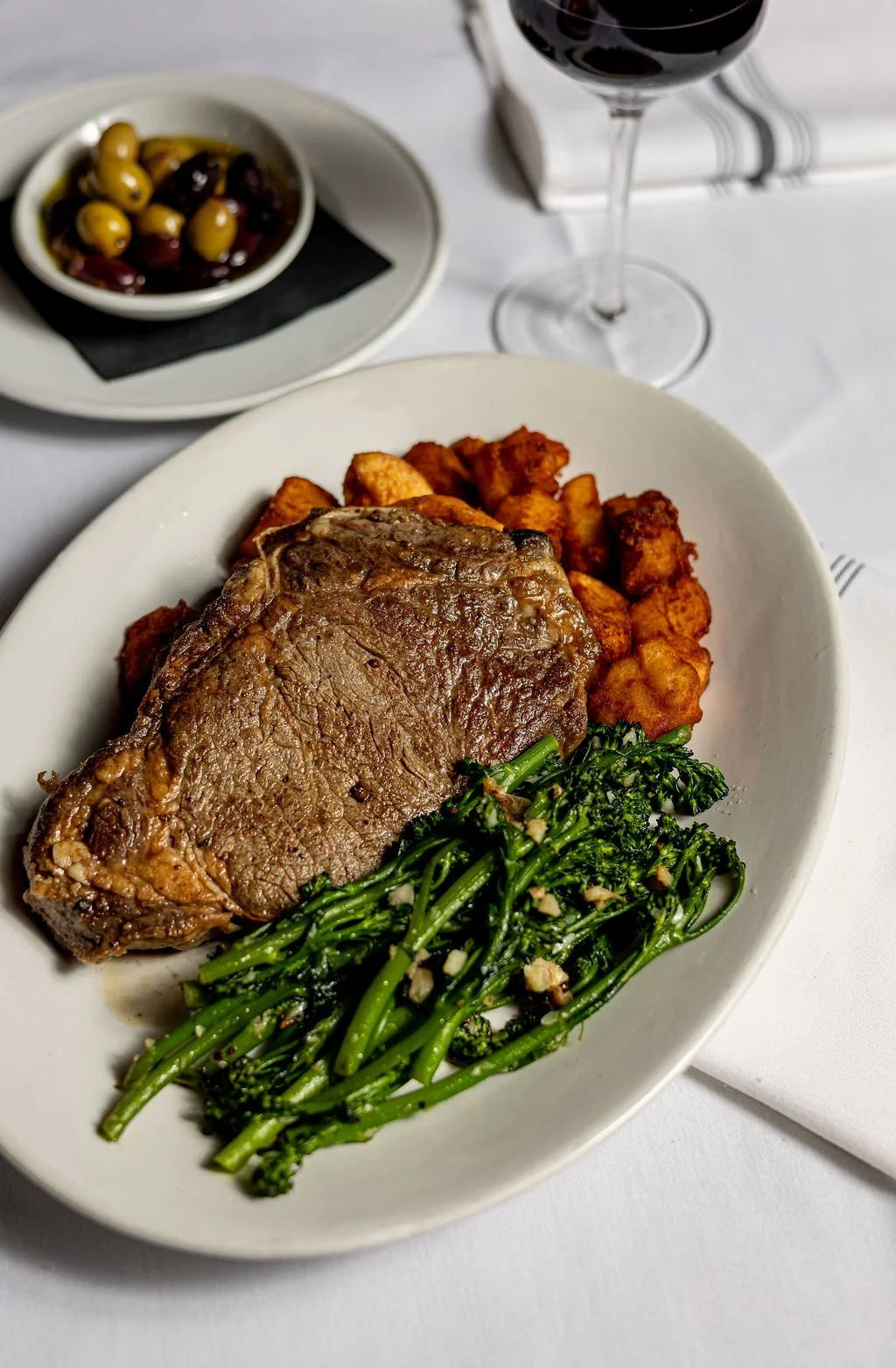 A plate with a cooked beef steak, roasted potatoes, and sautéed broccolini garnished with garlic.