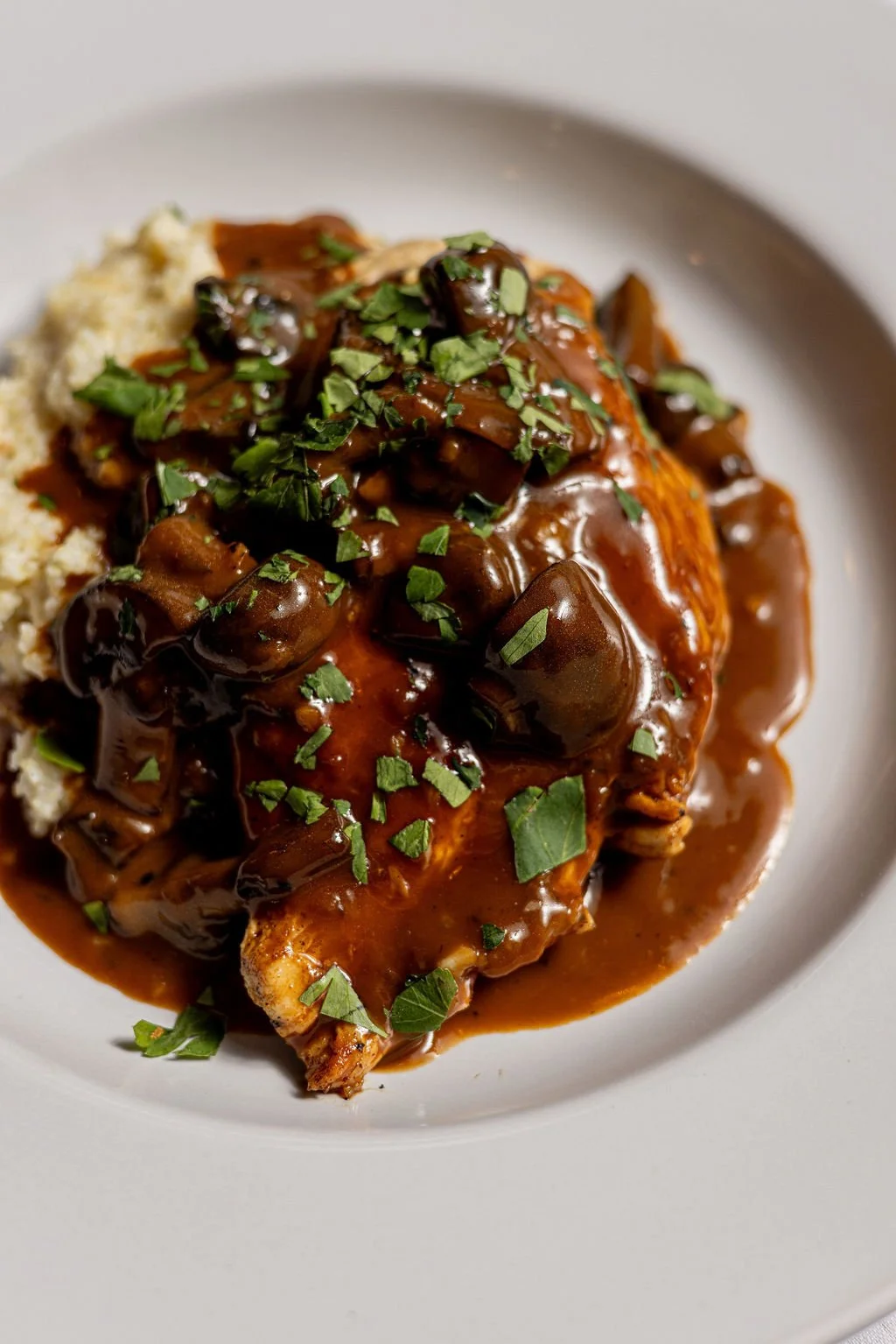 Plate of cooked chicken with mushroom gravy, garnished with chopped herbs, served with mashed potatoes.