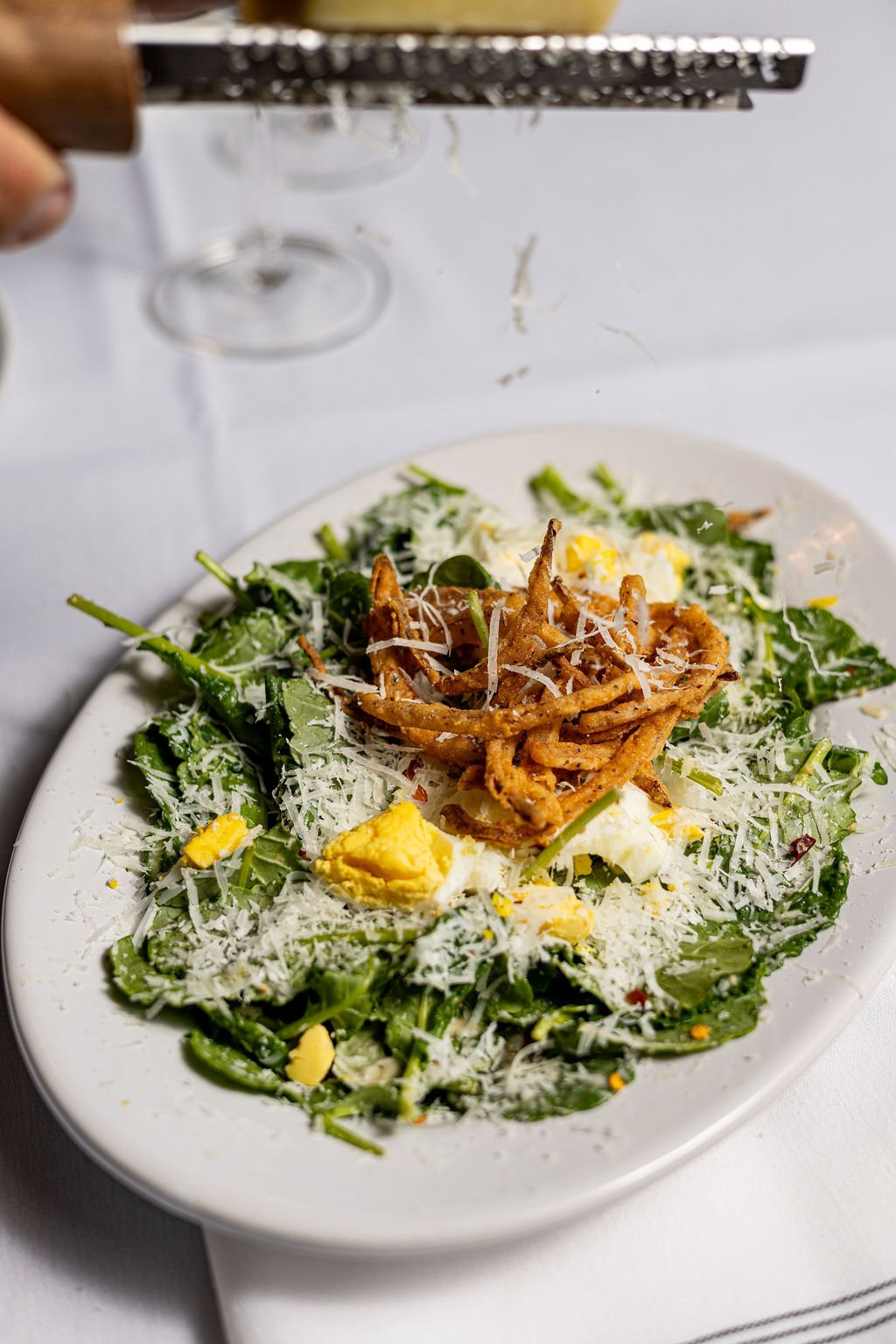 A salad with greens, hard-boiled eggs, shredded cheese, and fried onion strings on a white plate.