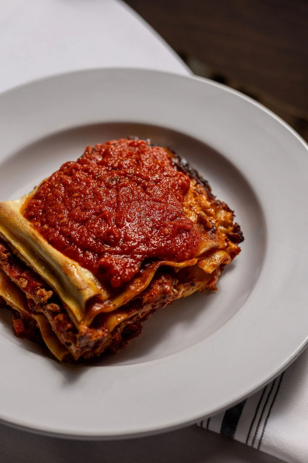 A serving of baked lasagna with tomato sauce on top on a white plate