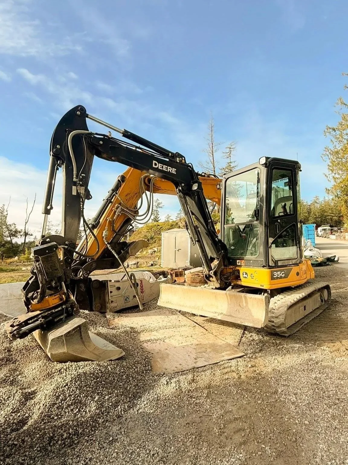 An excavator working at a construction site with blue sky and trees in the background.