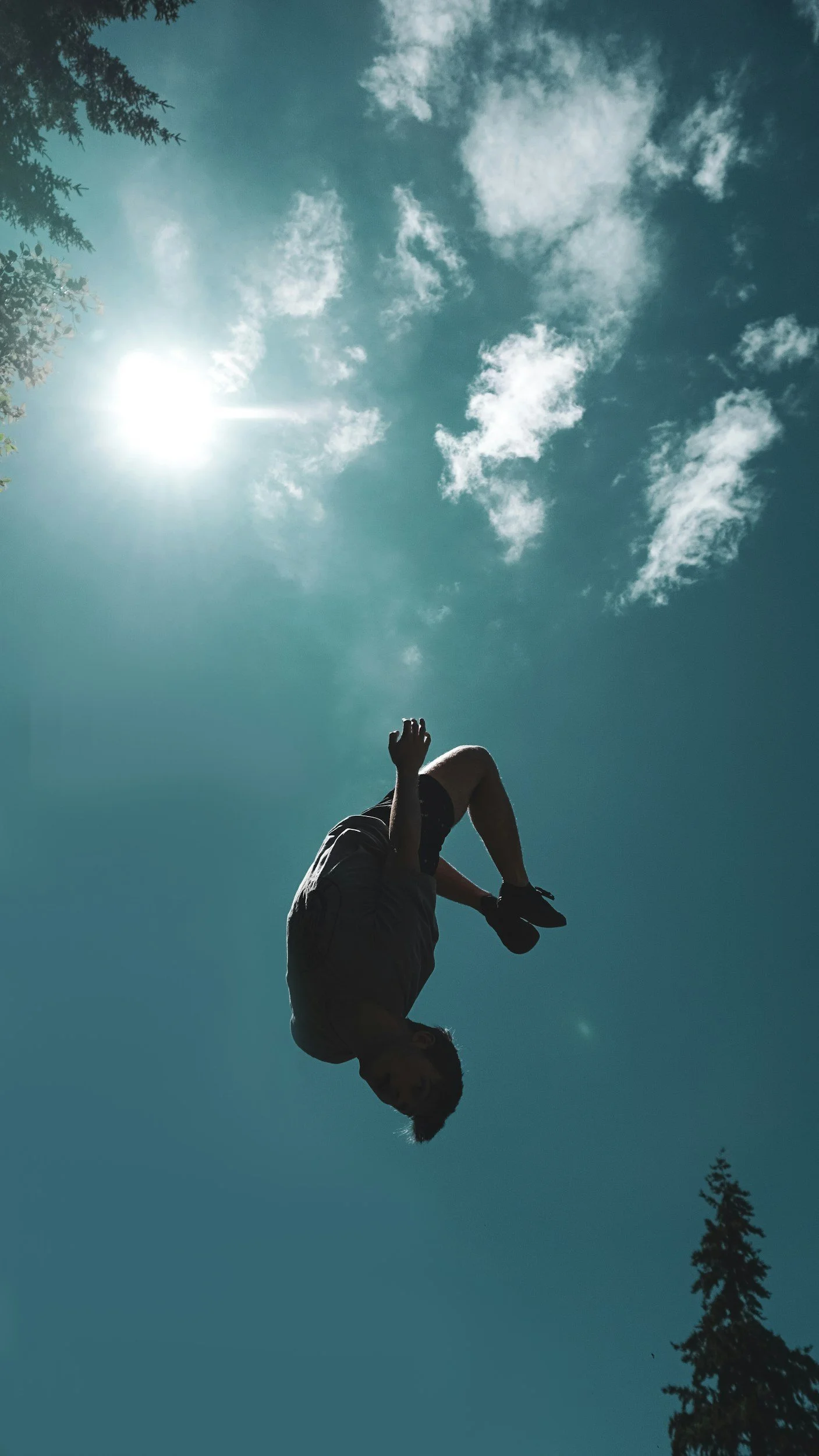 A person in mid-air against a bright blue sky with clouds, with the sun shining.