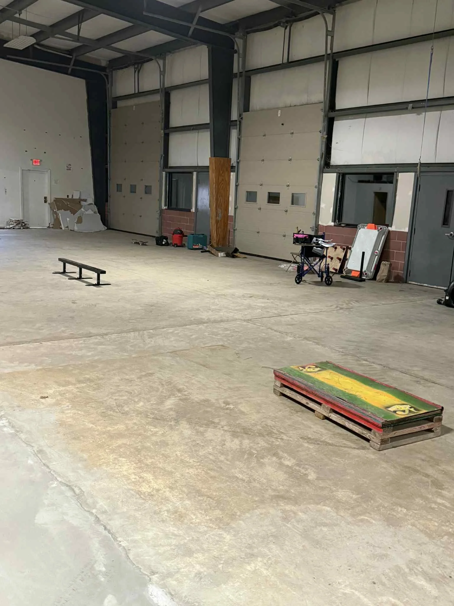 Empty industrial warehouse with some tools, pallets, and equipment scattered around.