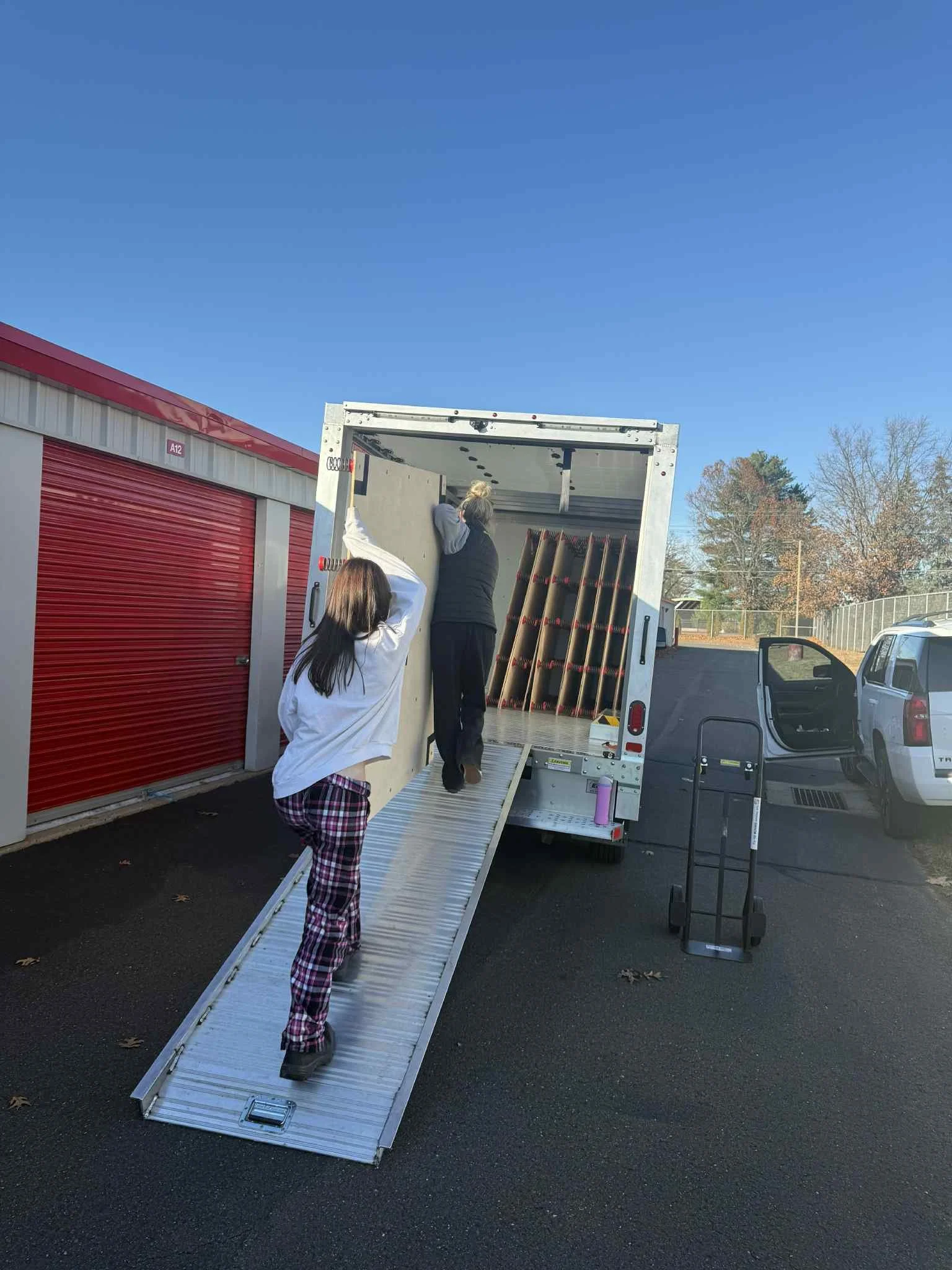 Two women loading items into a moving truck at a storage facility on a clear day.