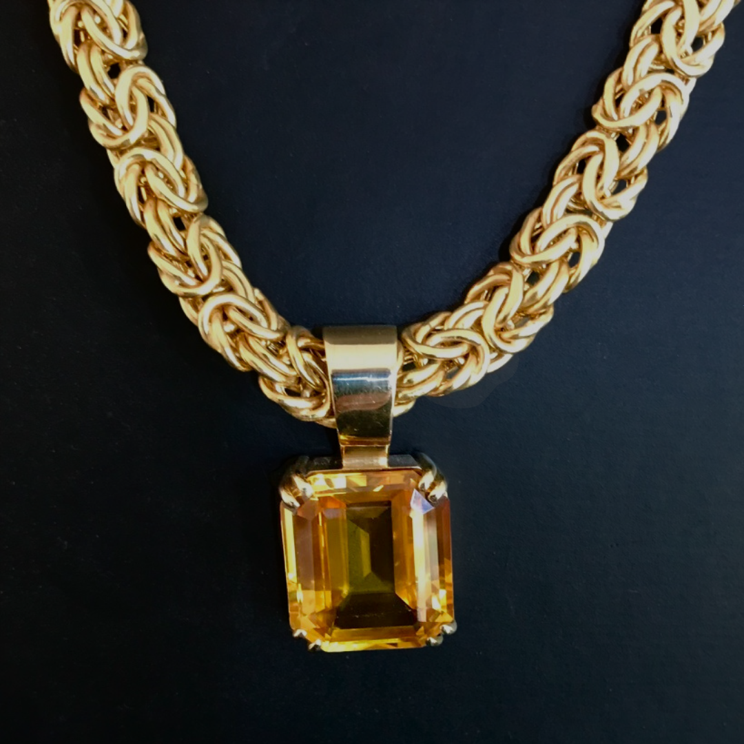 Gold chain necklace with a large rectangular yellow gemstone pendant on a black background.