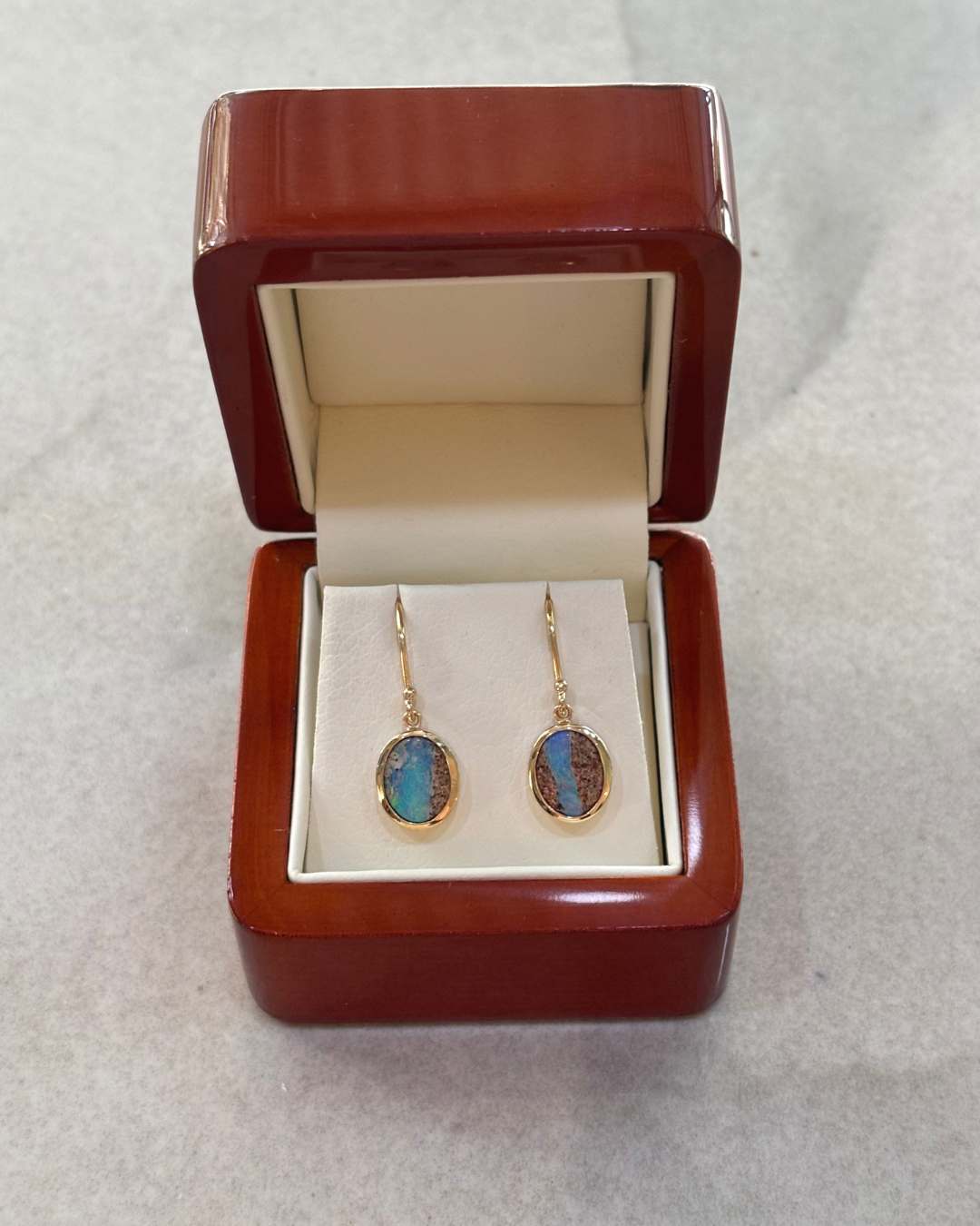 Gold earrings with oval multicoloured stones in a white jewellery box.