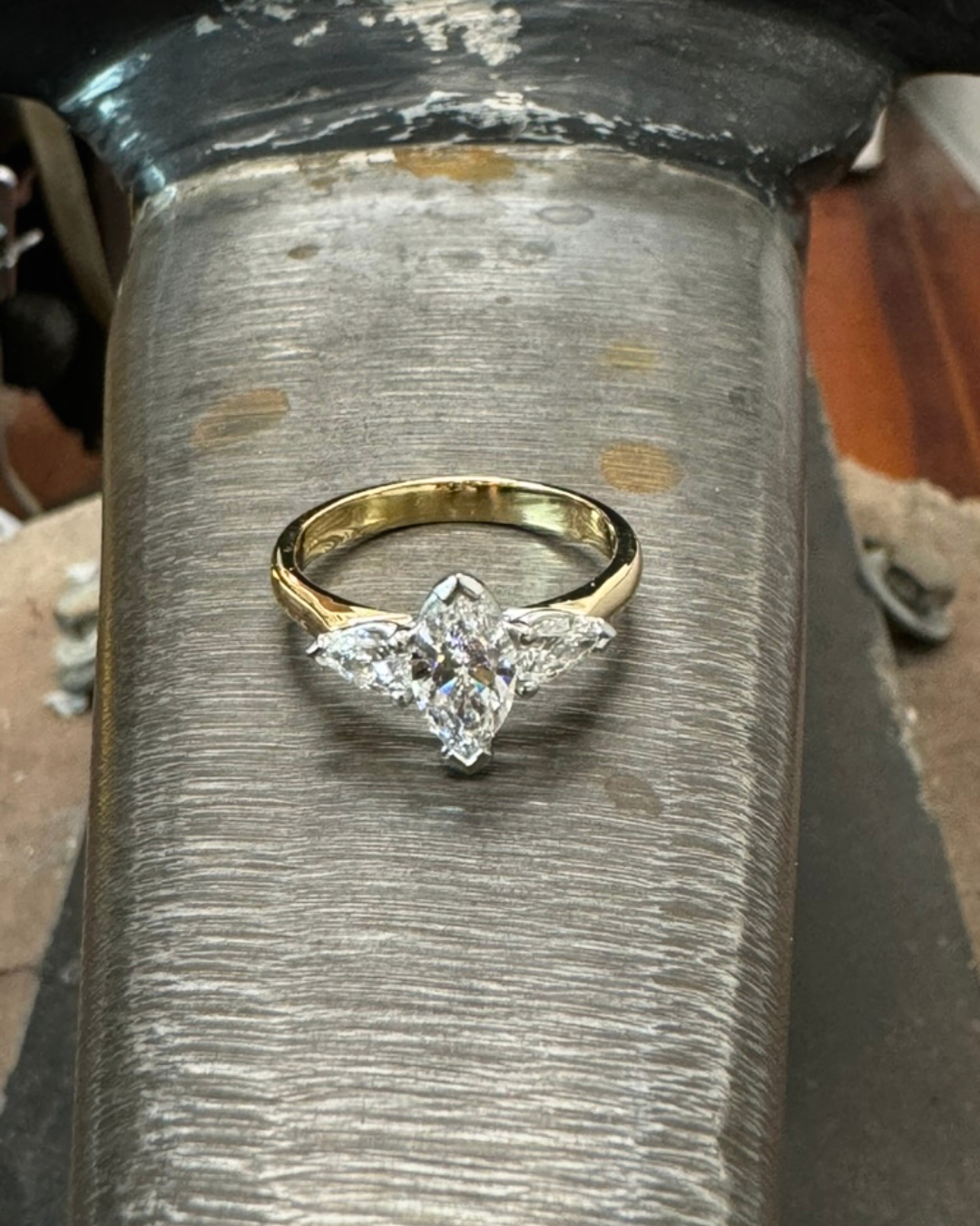 A gold ring with a large marquise-shaped diamond and smaller diamonds on each side, placed on a textured metal surface.
