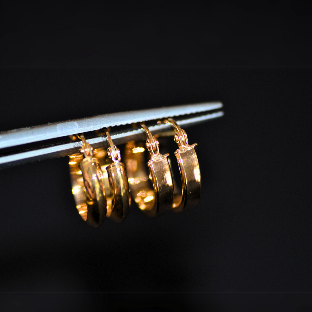 Close-up image of small gold hoop earrings hanging on a metallic display rod, with a black background.