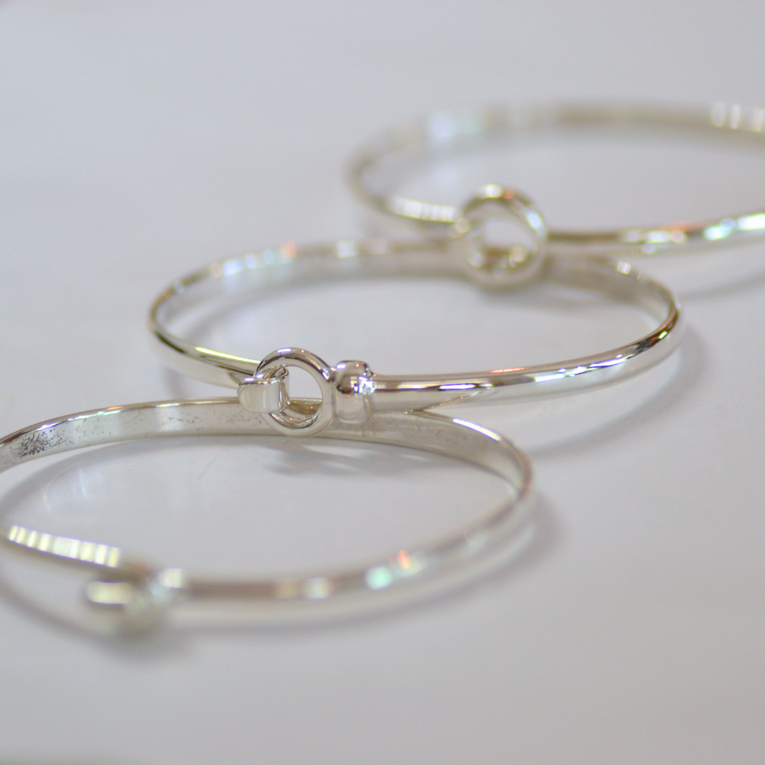 Close-up of three silver bangle bracelets with small circular details, placed on a white surface.