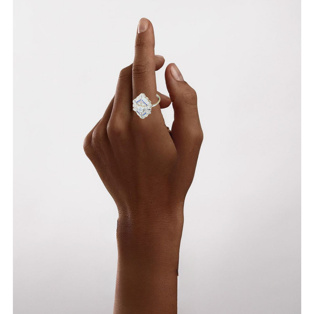 A person with brown skin wearing a ring with a large, shiny, intricate design.