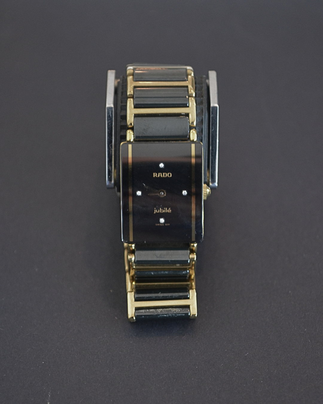 A black and gold wristwatch with a rectangular face and a metallic strap, displaying the brand name 'RADO' and the word 'jubile' on the dial.