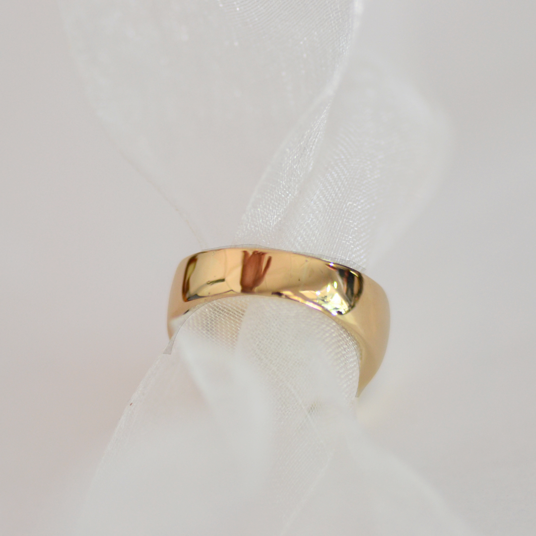 Close-up of a gold wedding band resting on white fabric.