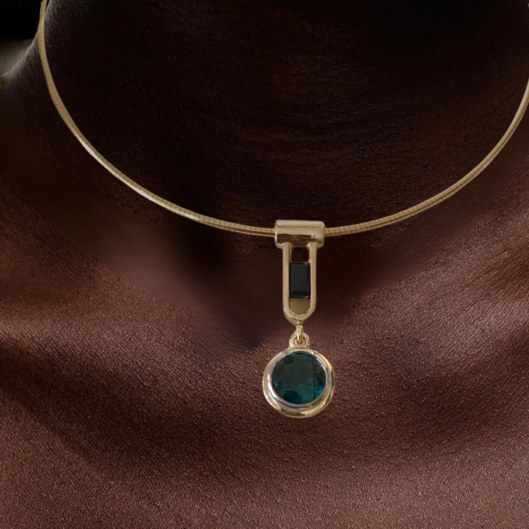 A close-up of a person's neck wearing a gold necklace with a black and green gemstone pendant.