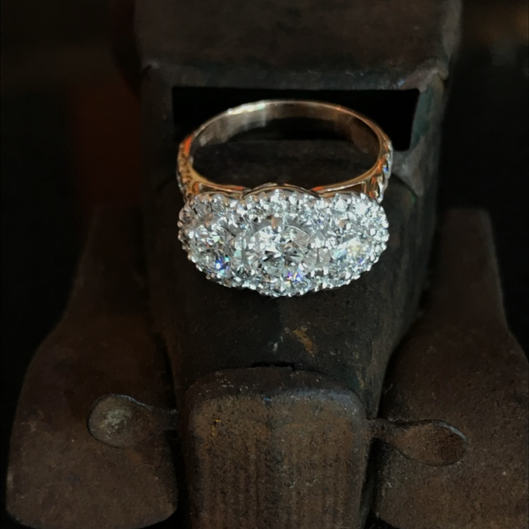 A silver ring with a large cluster of diamonds resting on a rusty metal surface.