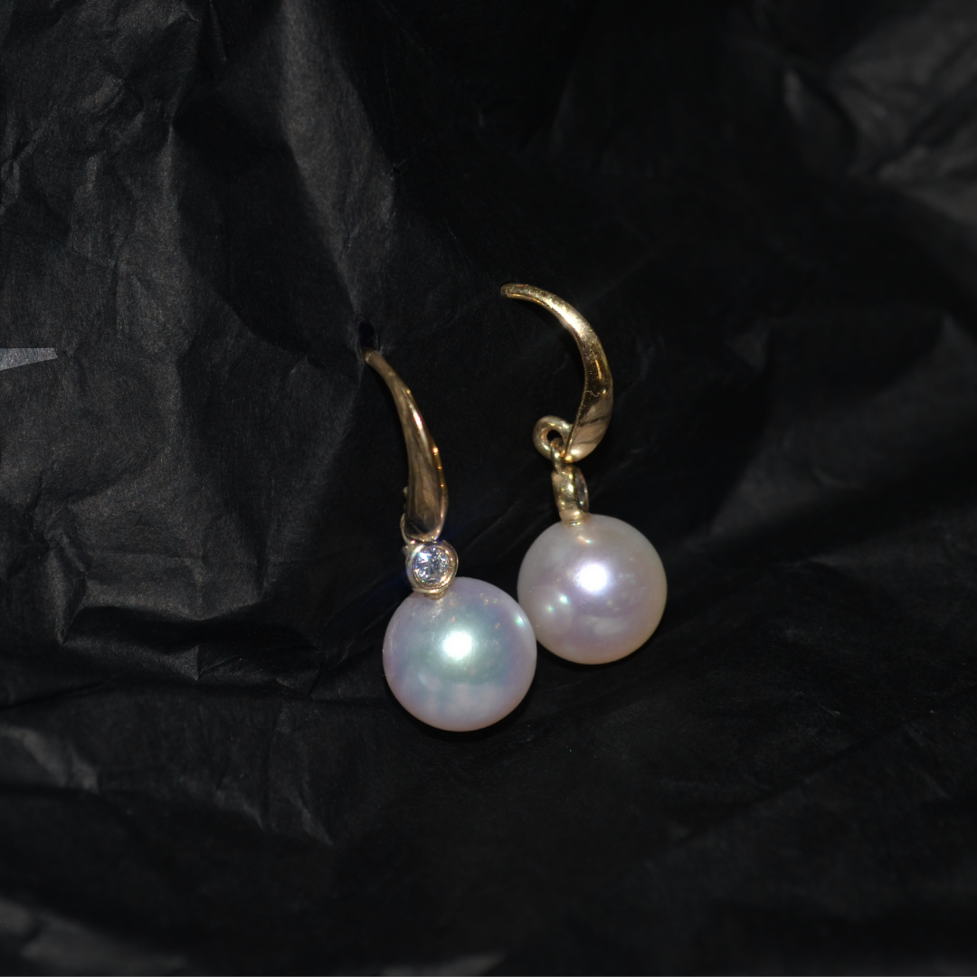 Gold earrings with large white pearls resting on black tissue paper.