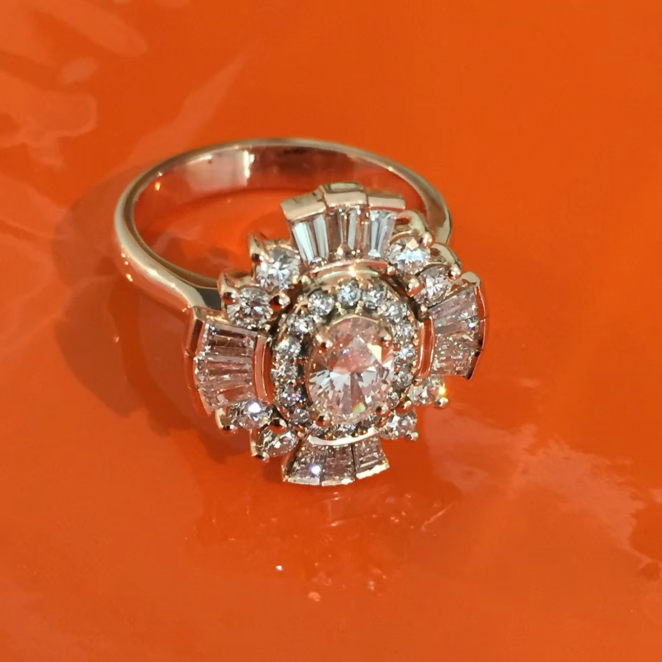 Silver ring with a large central diamond surrounded by smaller diamonds, on an orange surface.