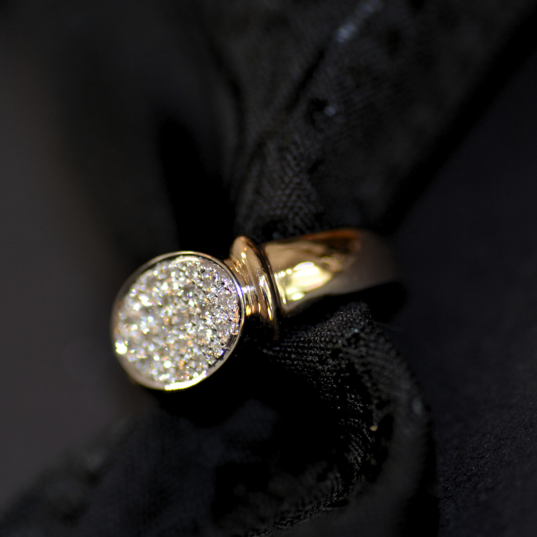 Close-up of a gold ring with a diamond-encrusted top, resting on black fabric.