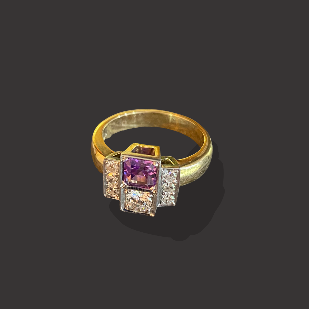 Gold ring with a central purple gemstone and surrounding diamonds on a dark background.