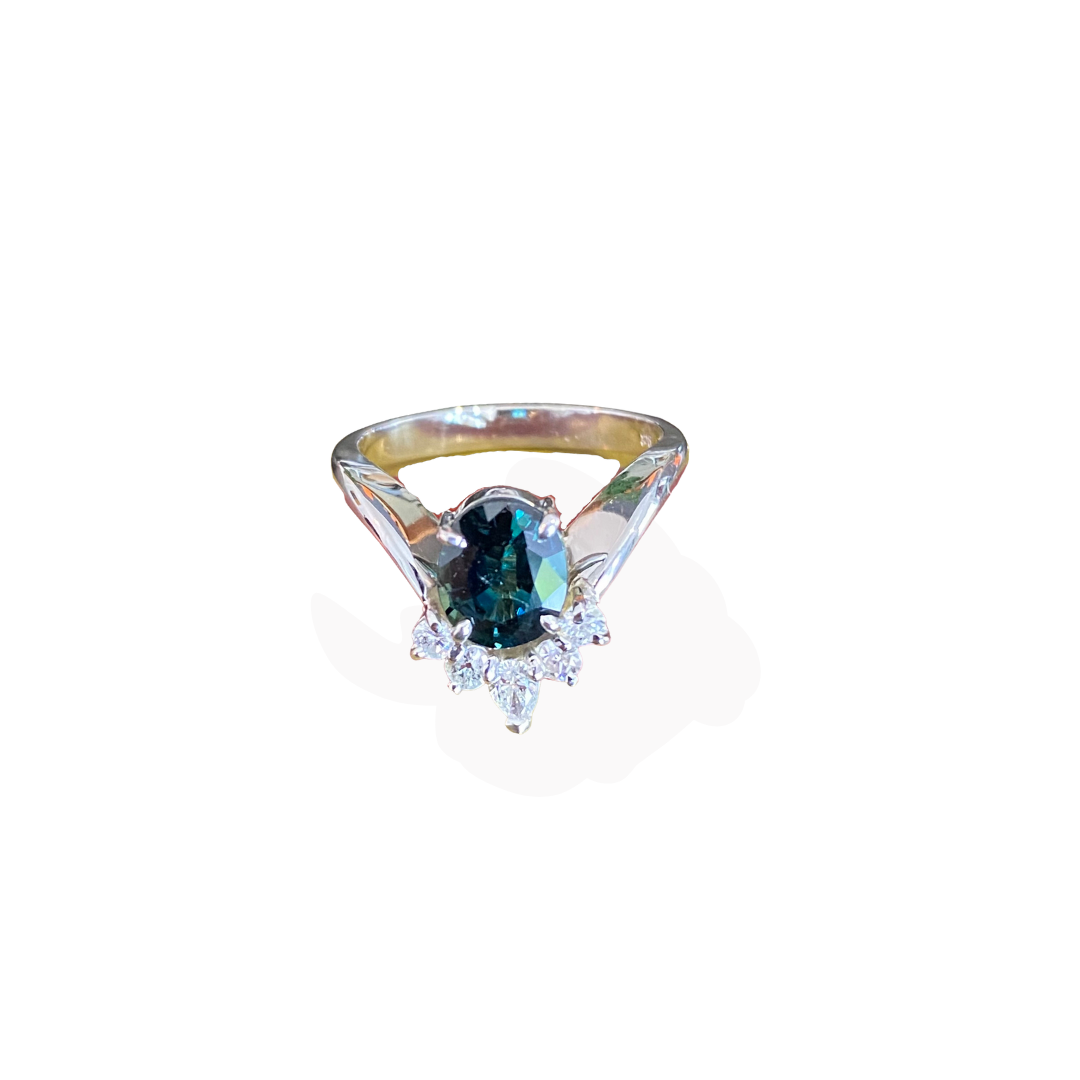 Gold ring with an oval dark green gemstone and surrounded by small clear diamonds.