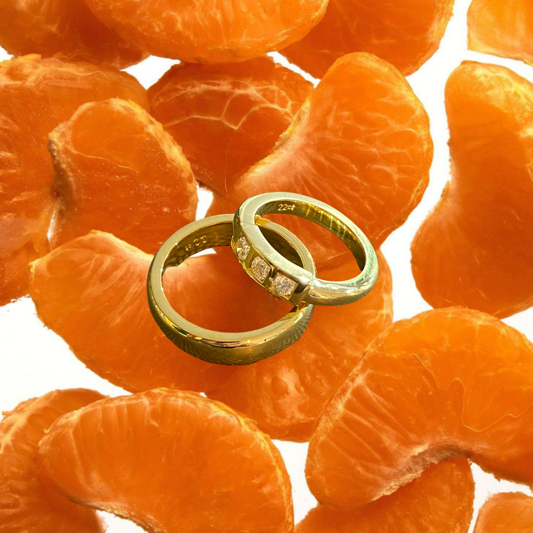 A close-up of two gold rings, one with embedded diamonds, placed on peeled orange tangerine segments.