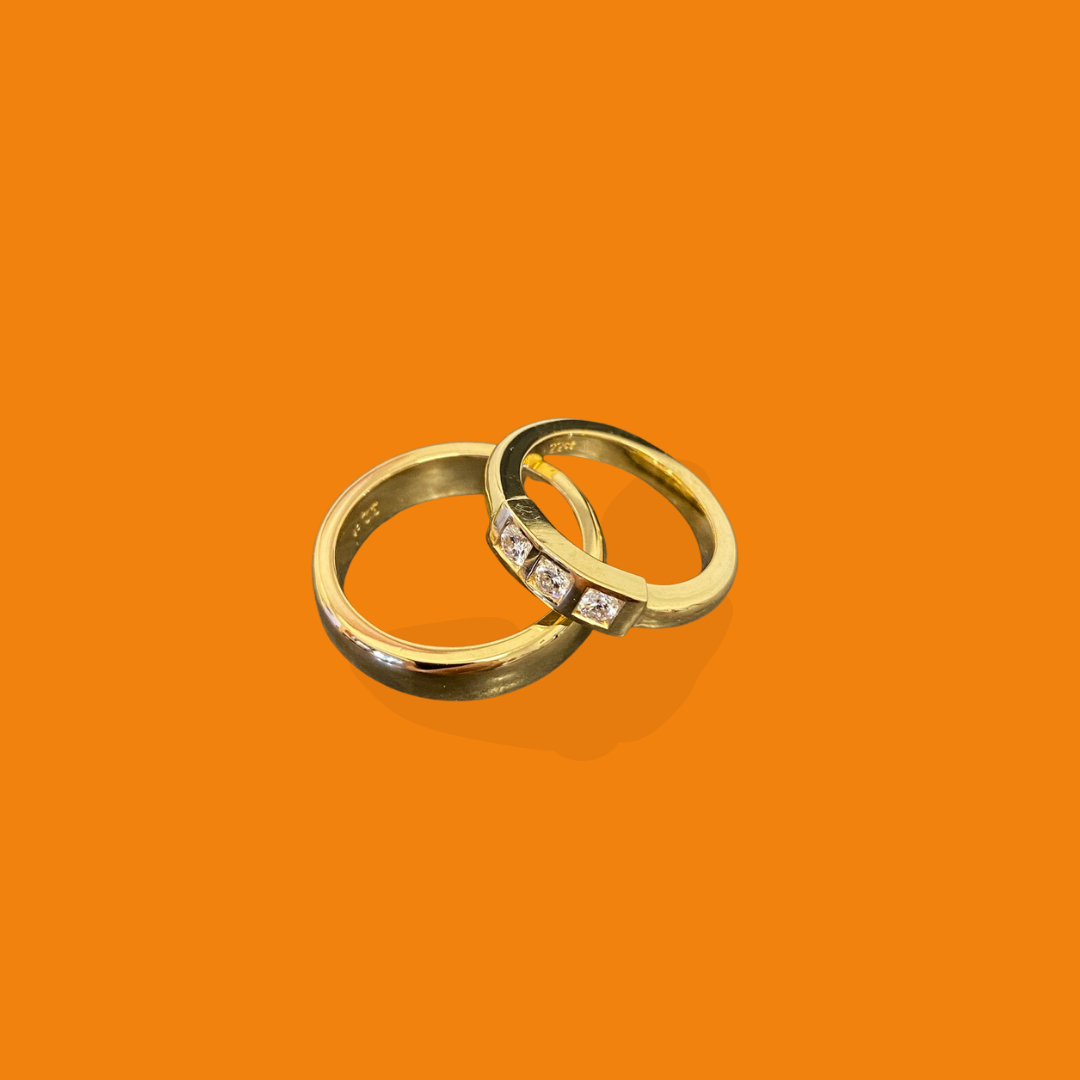 Two gold rings, one plain and one with small diamonds, on an orange background.