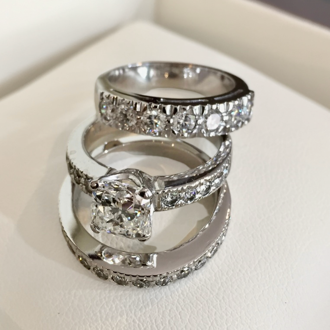 A close-up of four silver rings with diamonds, arranged on a white surface.