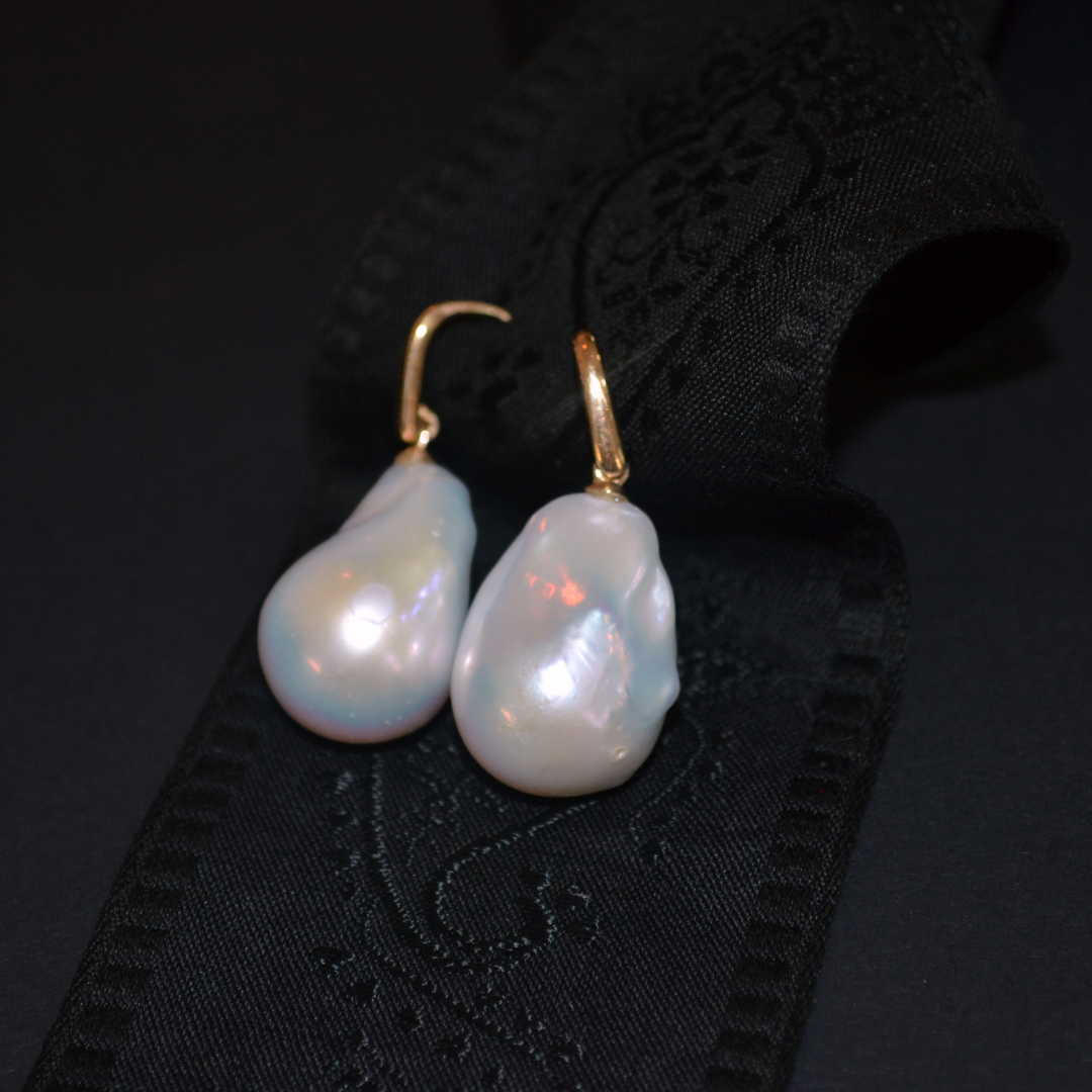 Pair of pearl earrings with gold hooks resting on black fabric.