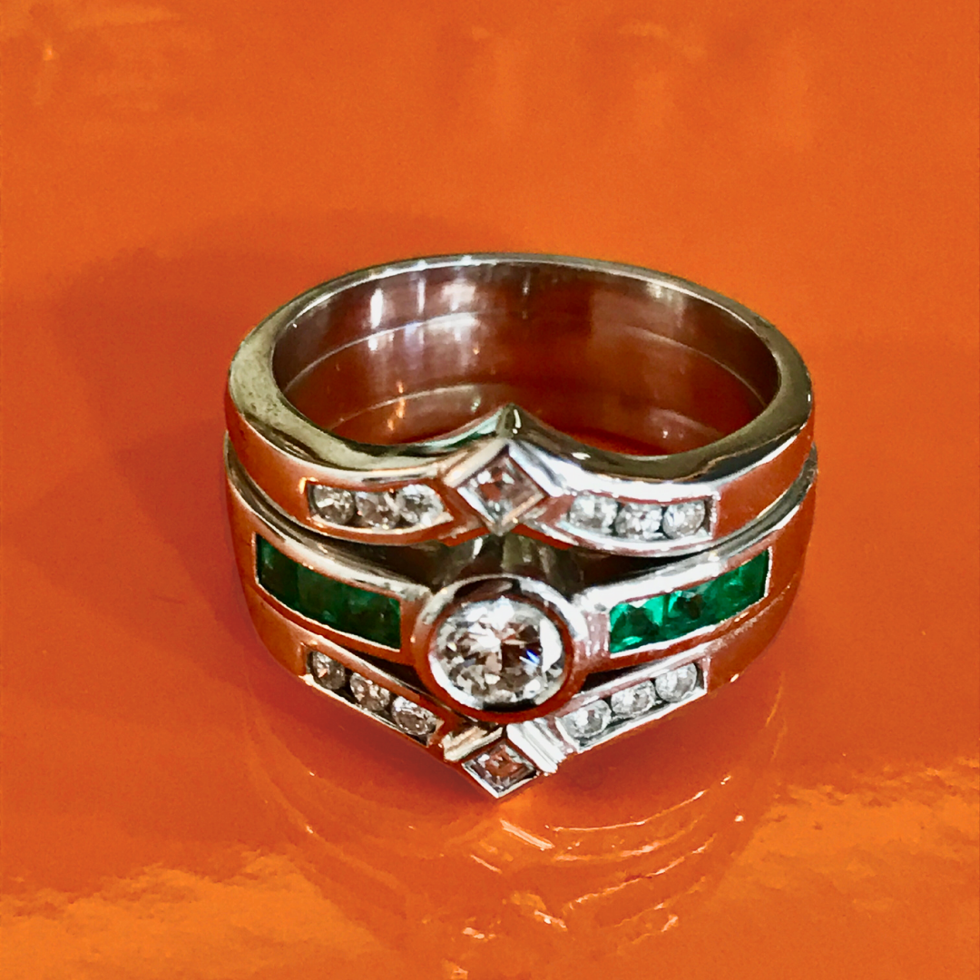 Silver ring with a large central diamond and green and clear smaller stones, on an orange background.
