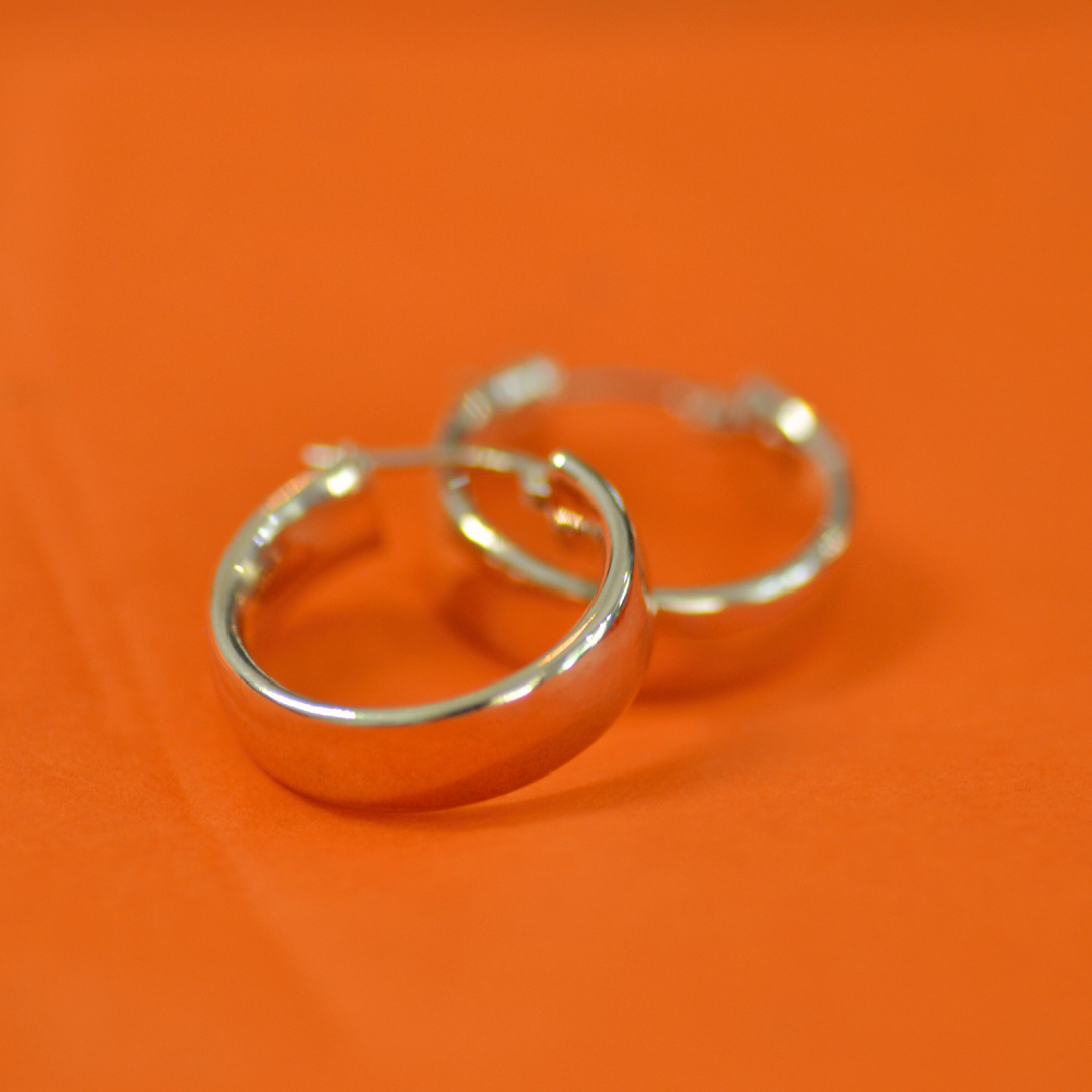 Pair of silver hoop earrings on an orange background.