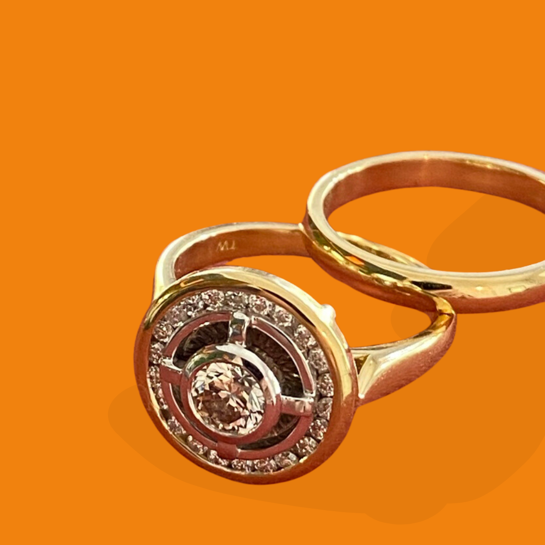 Close-up of a gold ring with a central diamond surrounded by smaller diamonds, resting on an orange background.