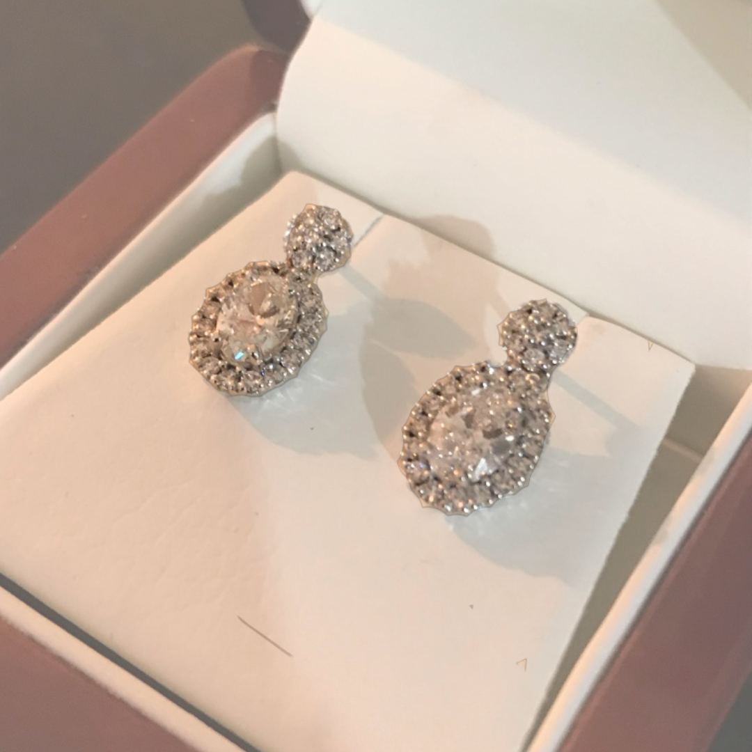 A pair of sparkling, round-shaped earrings with numerous small rhinestones, displayed in an open jewelry box with a white interior.
