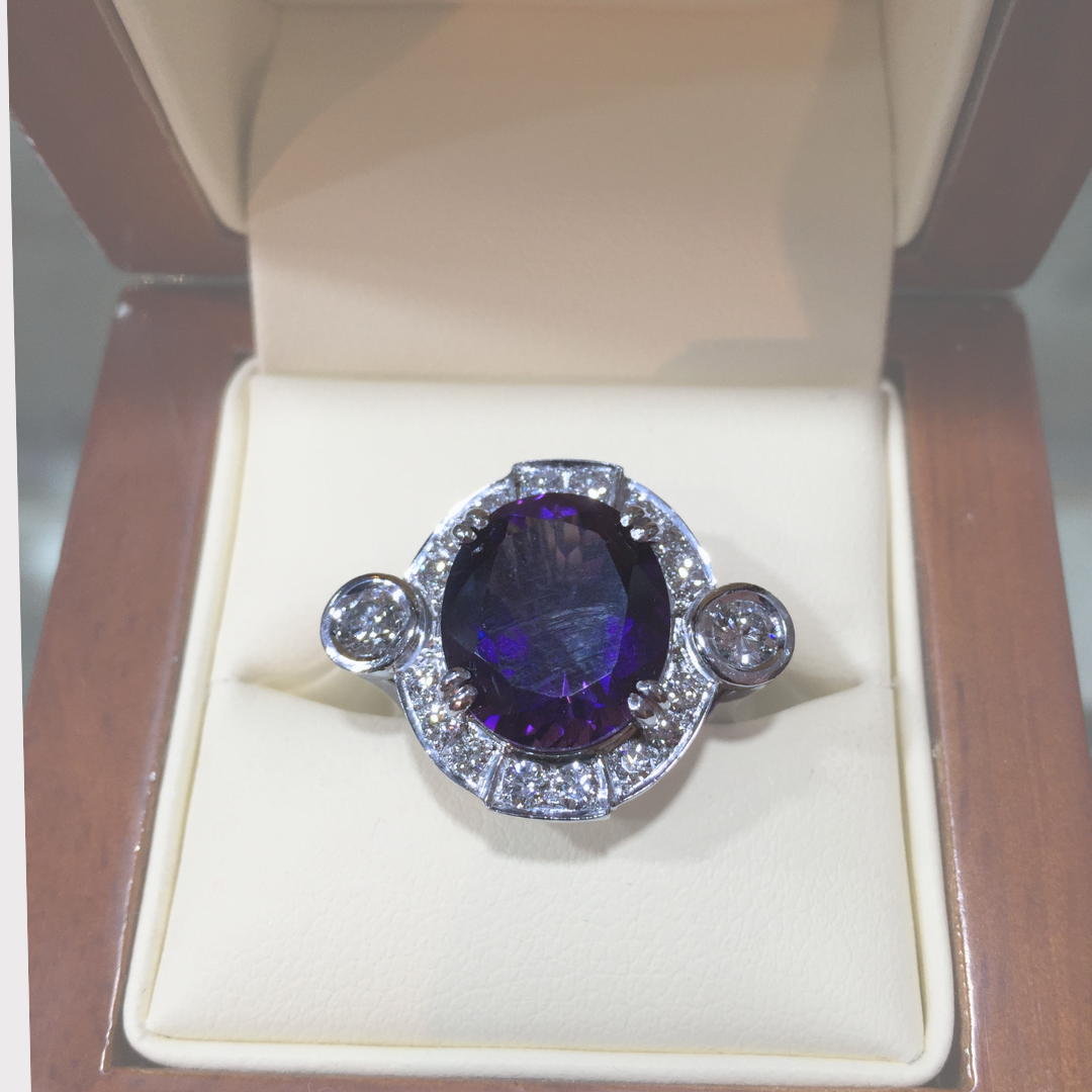 A ring with a large oval deep purple gemstone surrounded by smaller diamonds in a jewelry box.