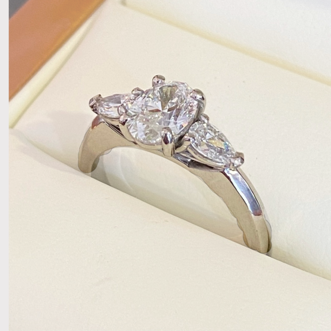 A silver ring with three large diamonds, in a white jewelry box.