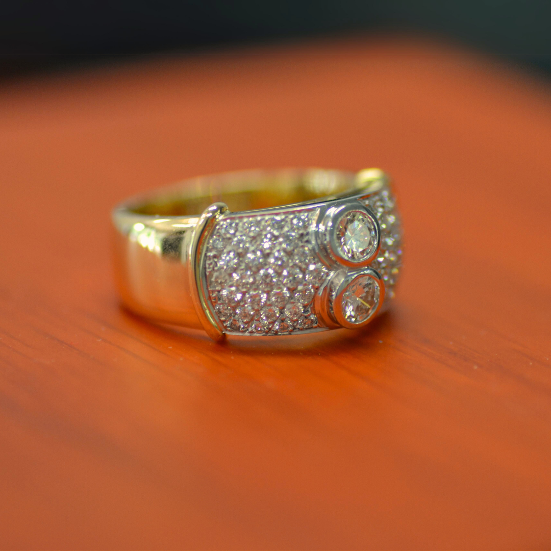 A silver ring with two embedded clear gemstones and numerous smaller diamonds set on the band, resting on a wooden surface.