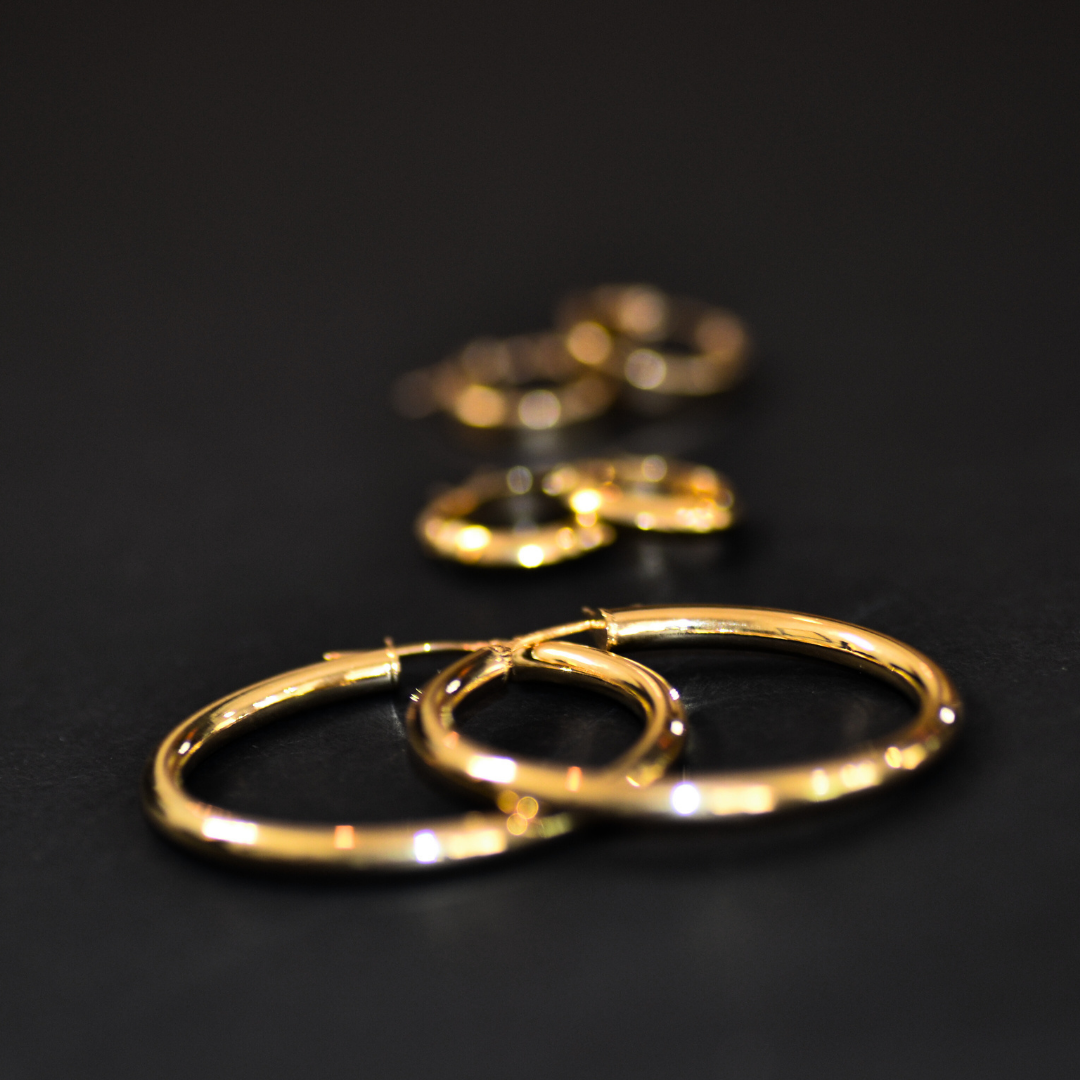 Close-up of gold hoop earrings and rings on a black surface.