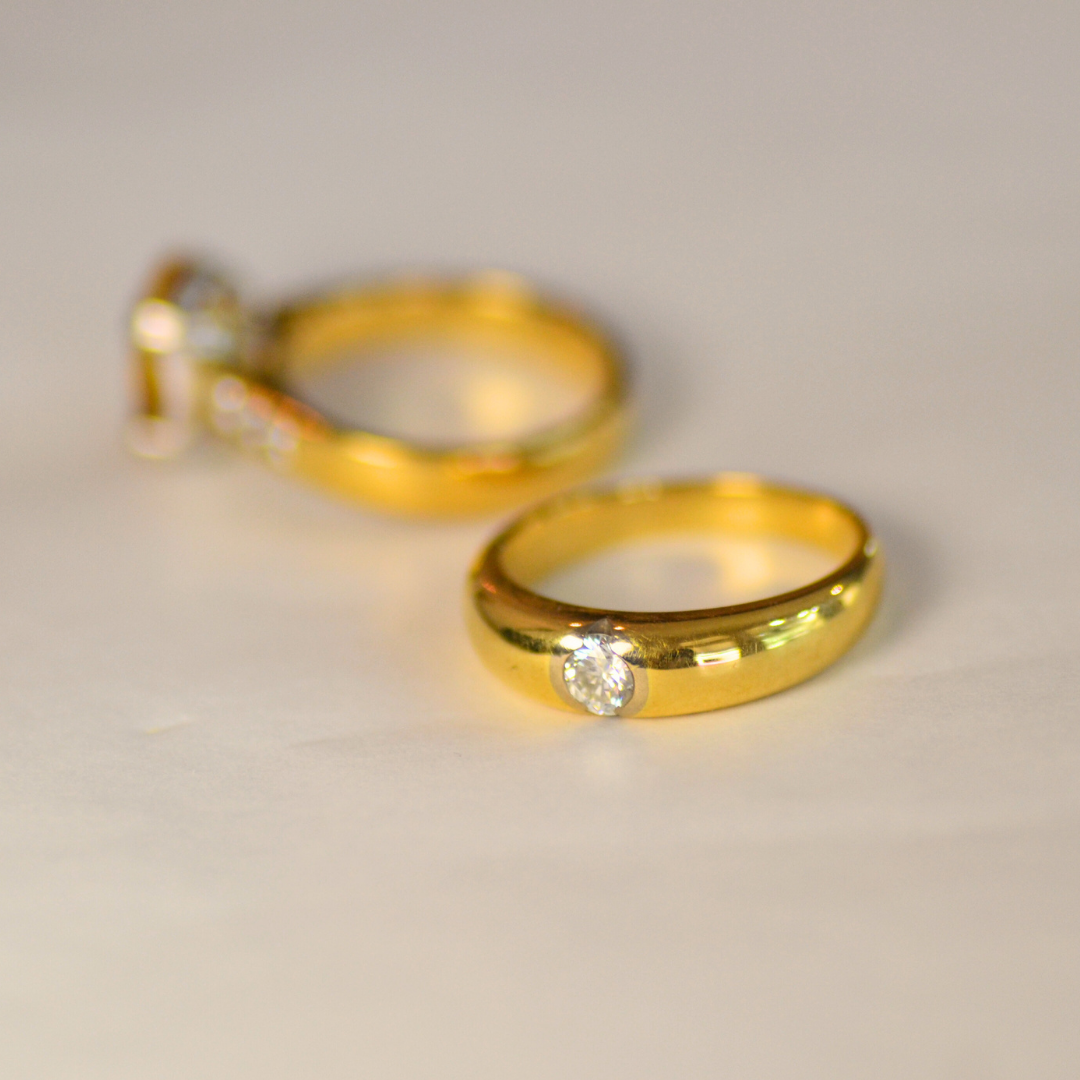 Close-up of two gold rings with a single diamond on each, placed on a white surface.