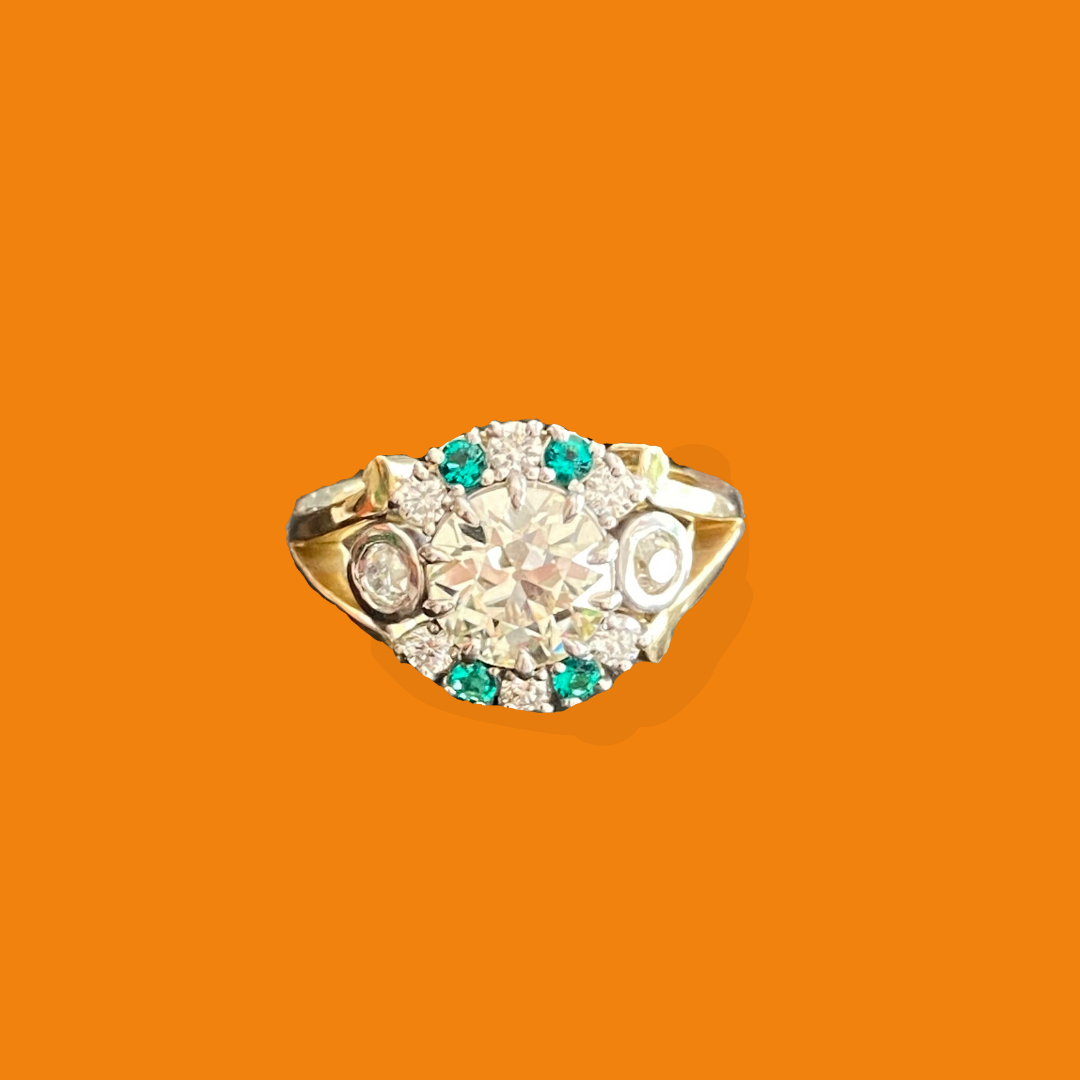 Close-up of a silver ring with a large central diamond surrounded by smaller diamonds and turquoise stones, set against an orange background.
