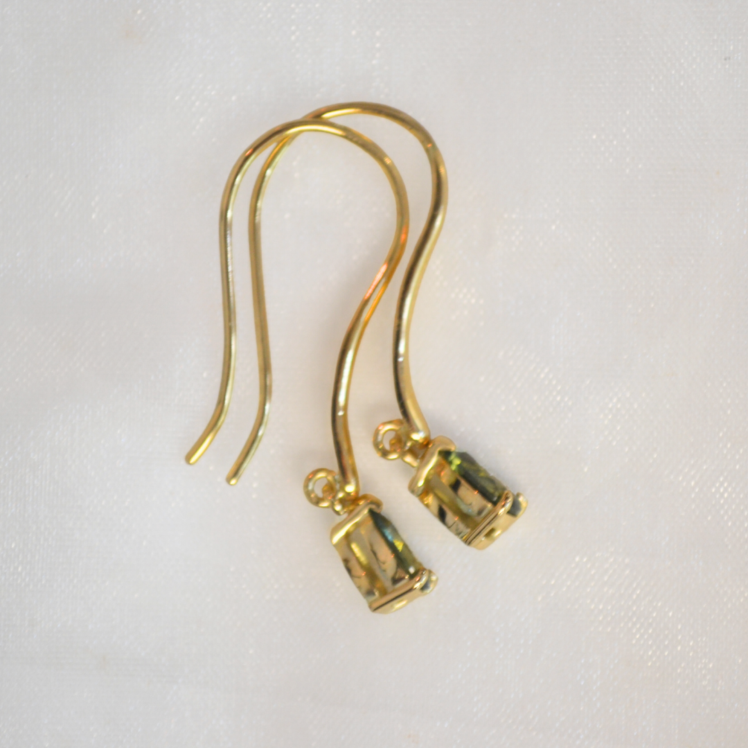 A pair of gold earrings with small cylindrical ends resting on a white textured surface.