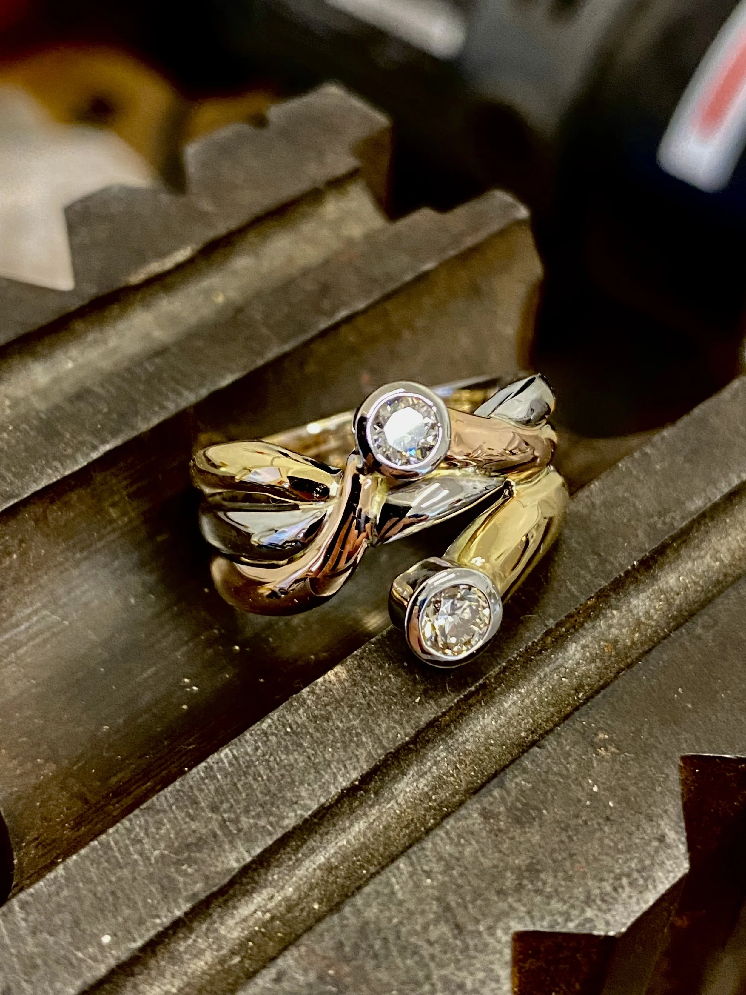 A gold ring with two diamonds, one round and one marquise, placed on a metal vise.