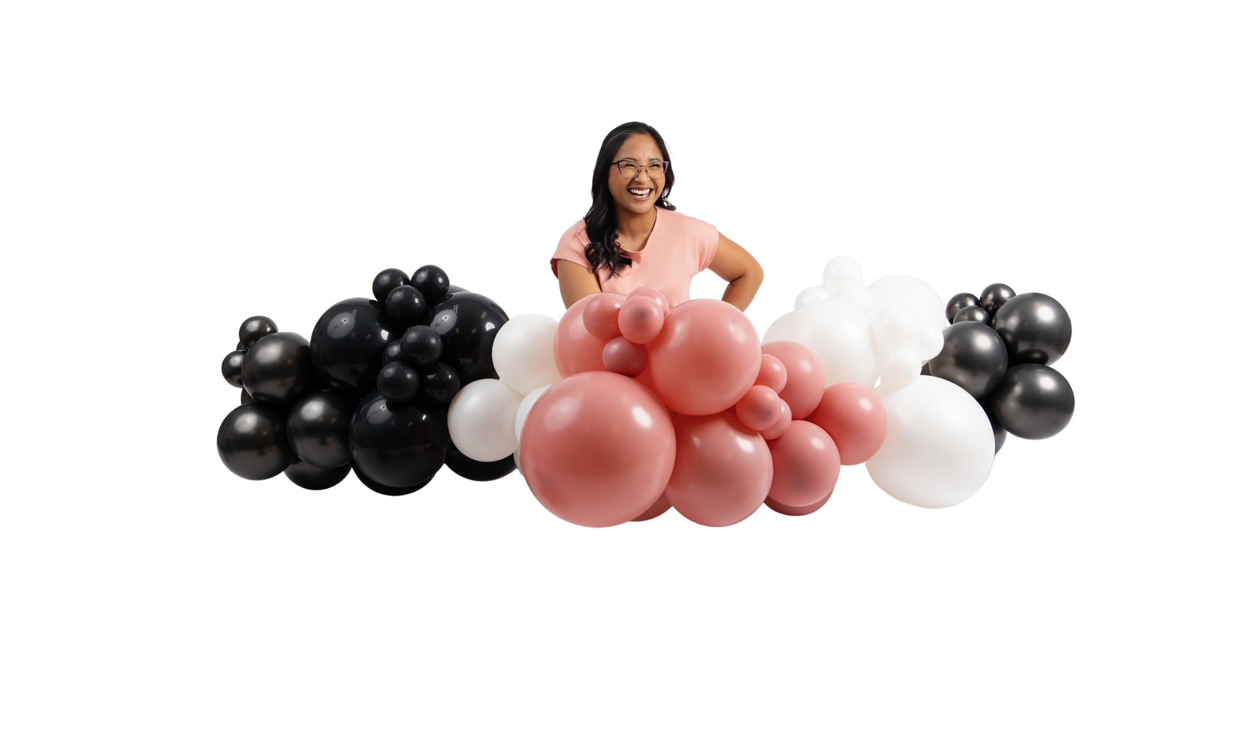 Owner smiling and sitting among clusters of balloons in black, white, and pink colors.