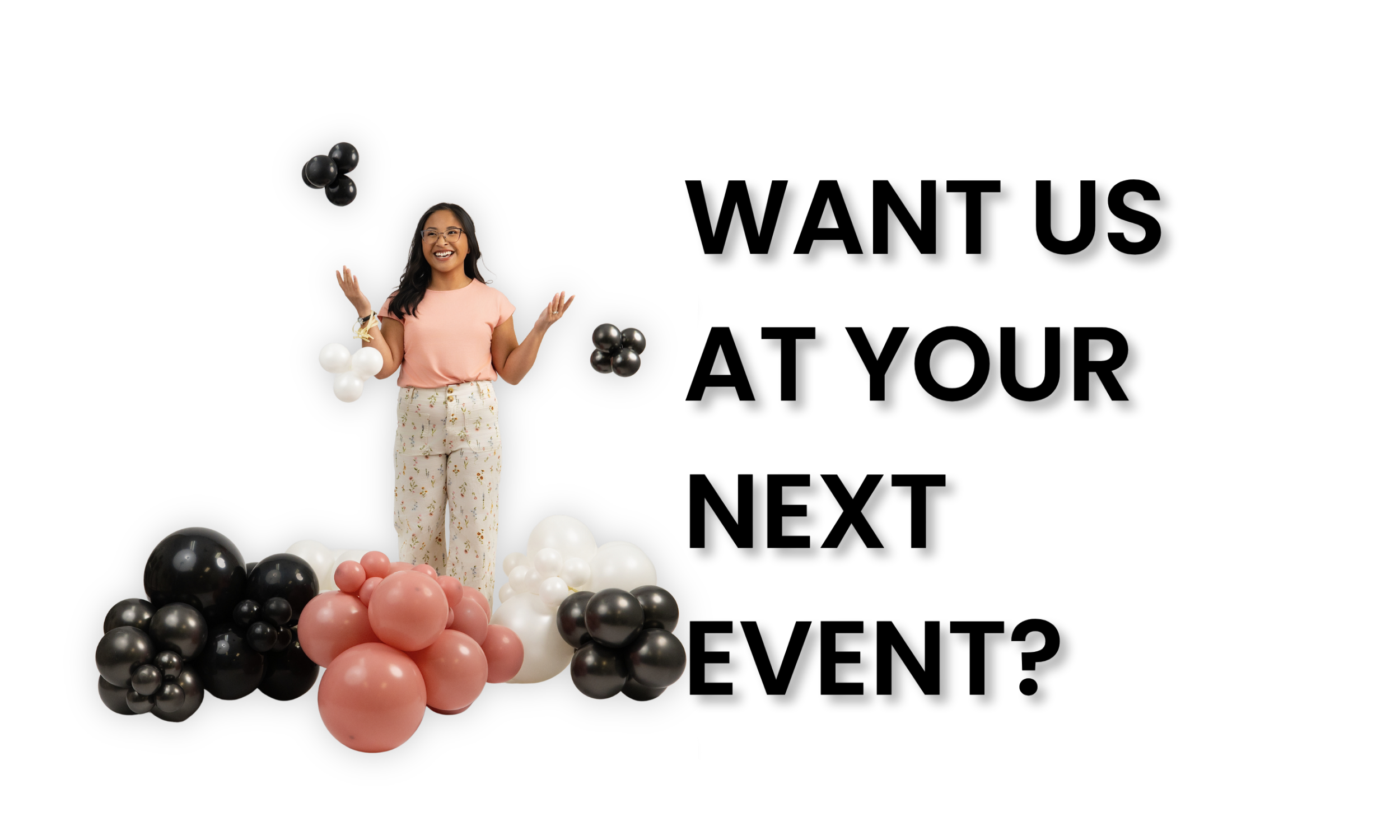Owner in pink shirt and floral pants standing amidst a variety of black, white, and pink balloons, smiling.