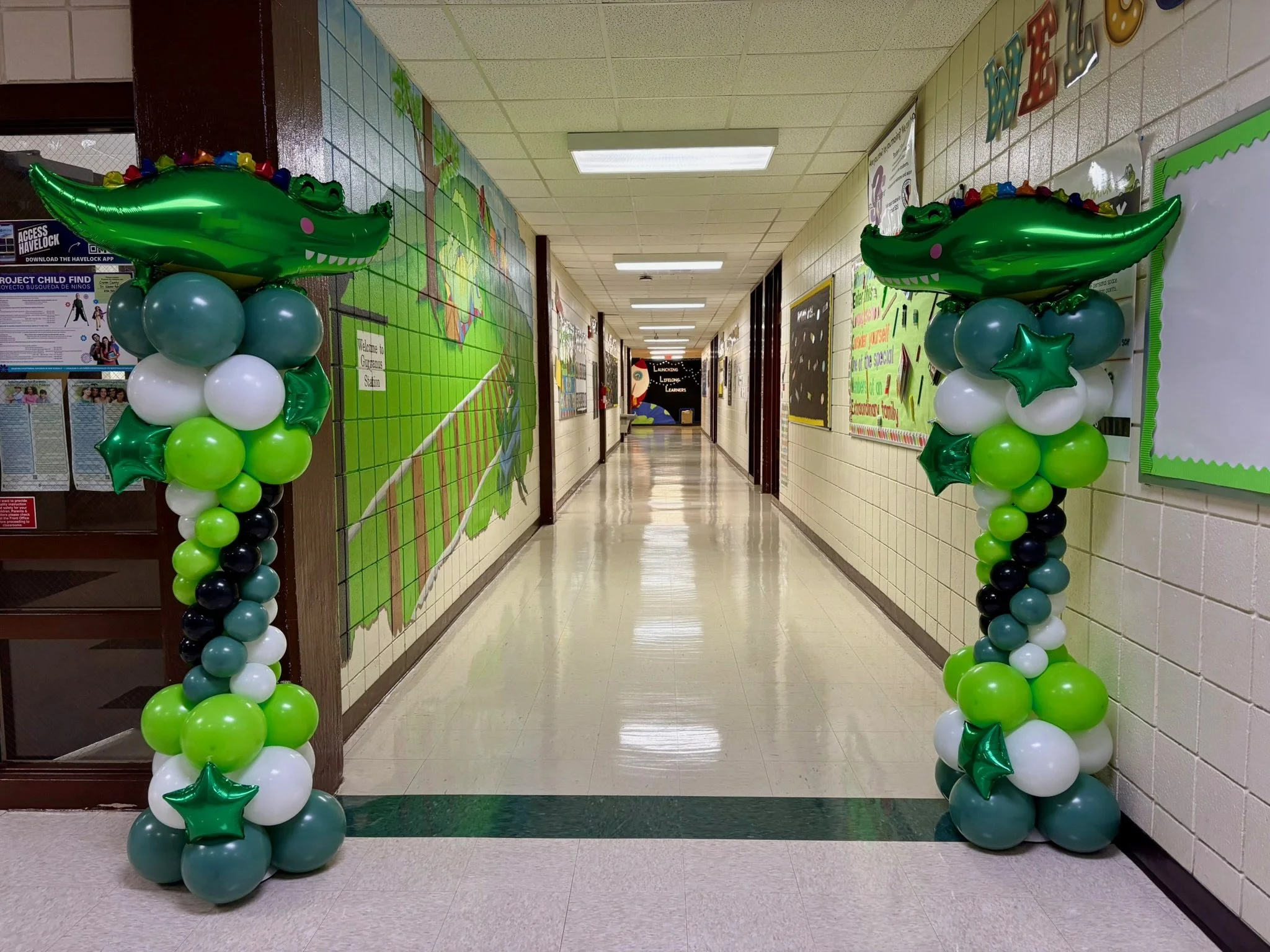 School hallway balloon arch with green dinosaur-themed balloon columns